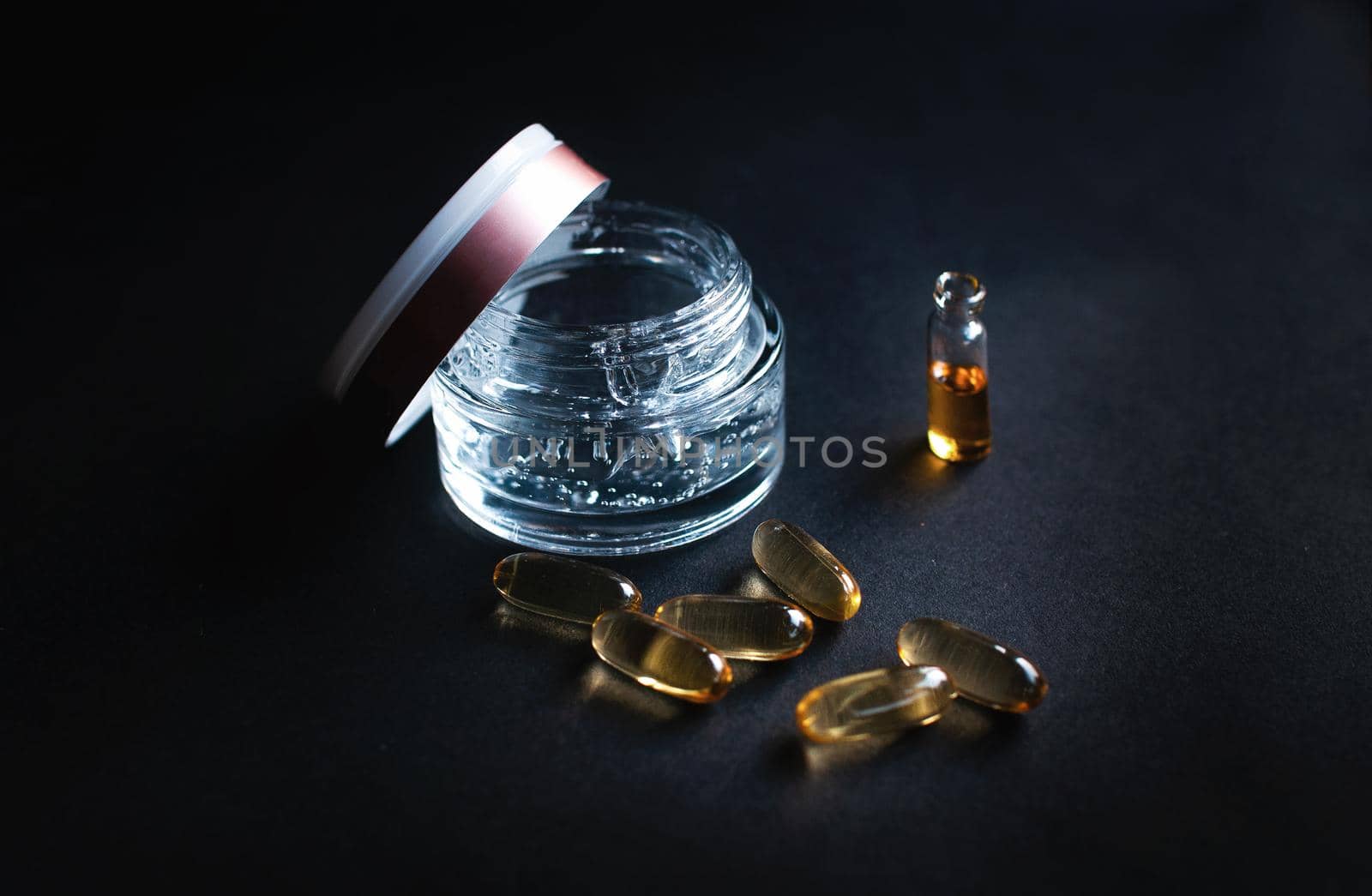 transparent jar with moisturizing cream with hyaluronic acid and vitamins in capsules on a black background