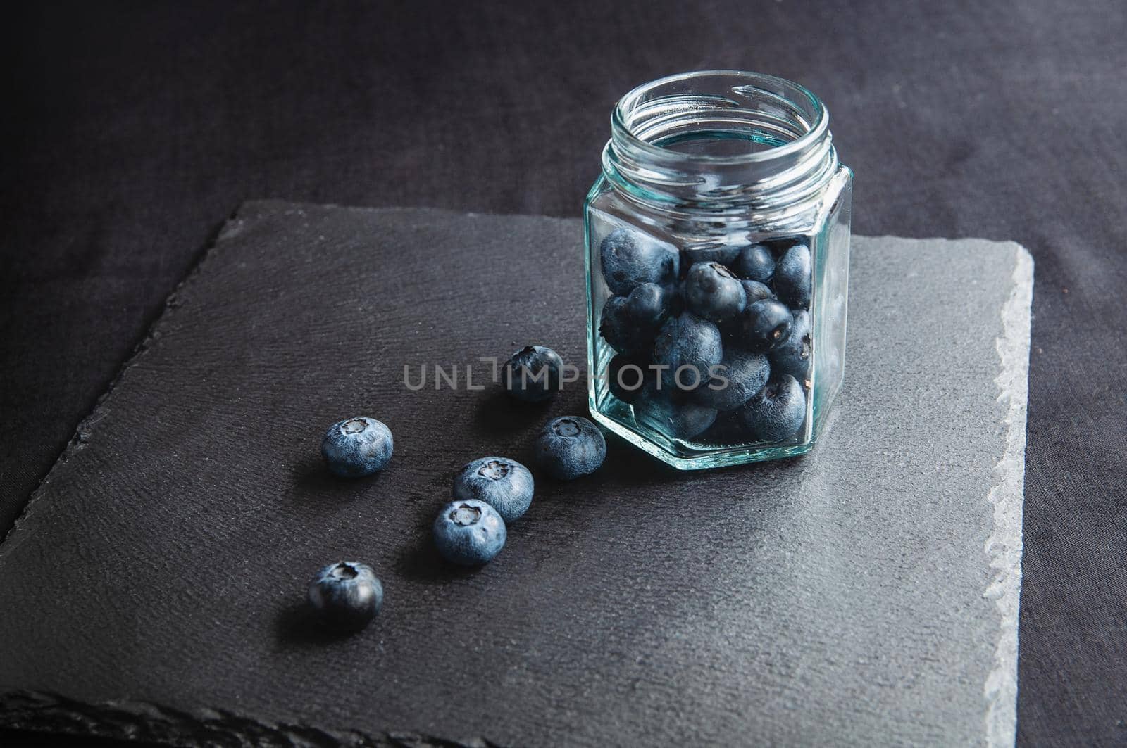 Fresh blueberries in a glass jar and laid out on a black board. Blueberries for a healthy diet and vegetarians