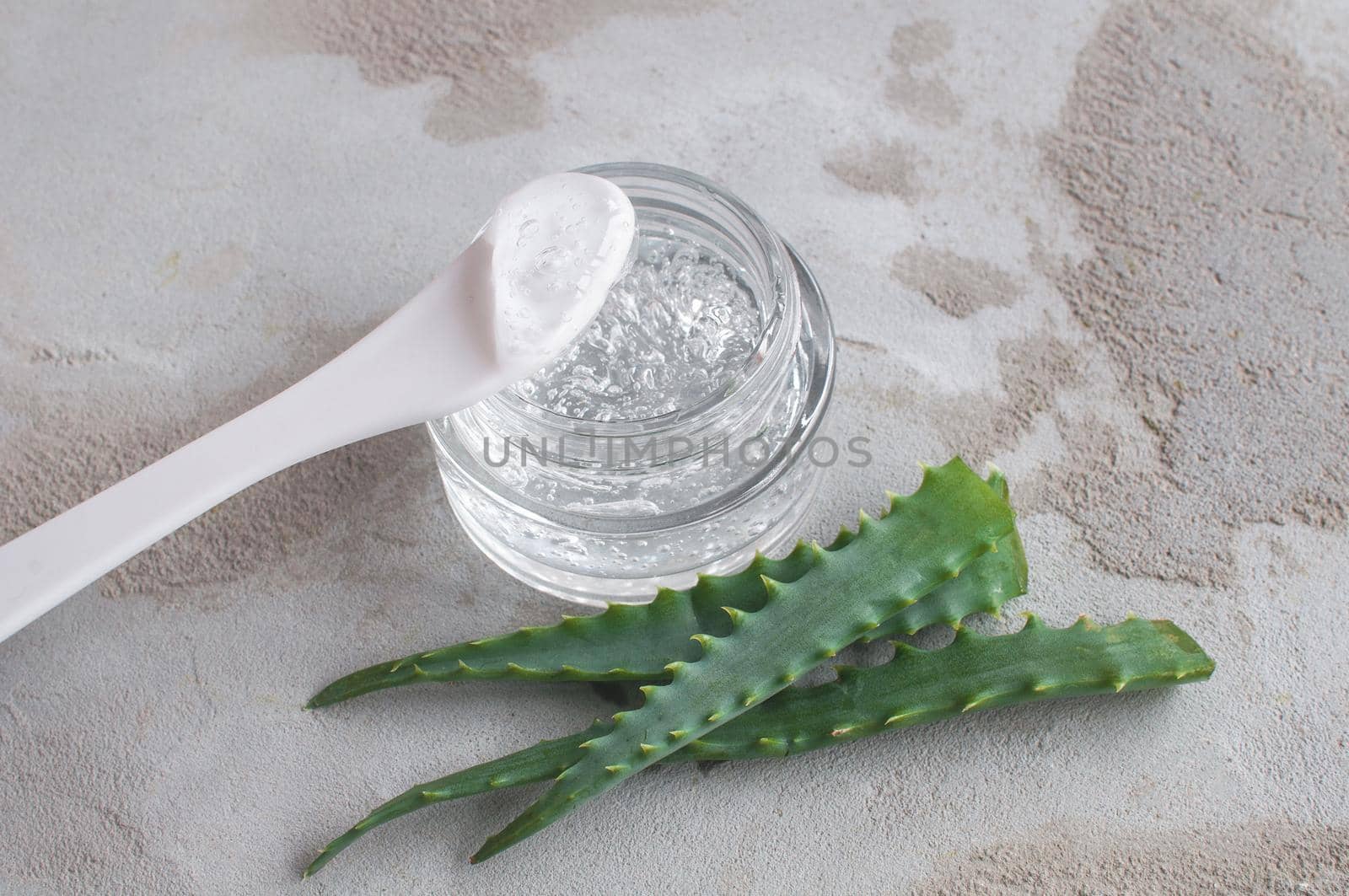 Gel with hyaluronic acid and aloe vera branches in a glass jar on a concrete background