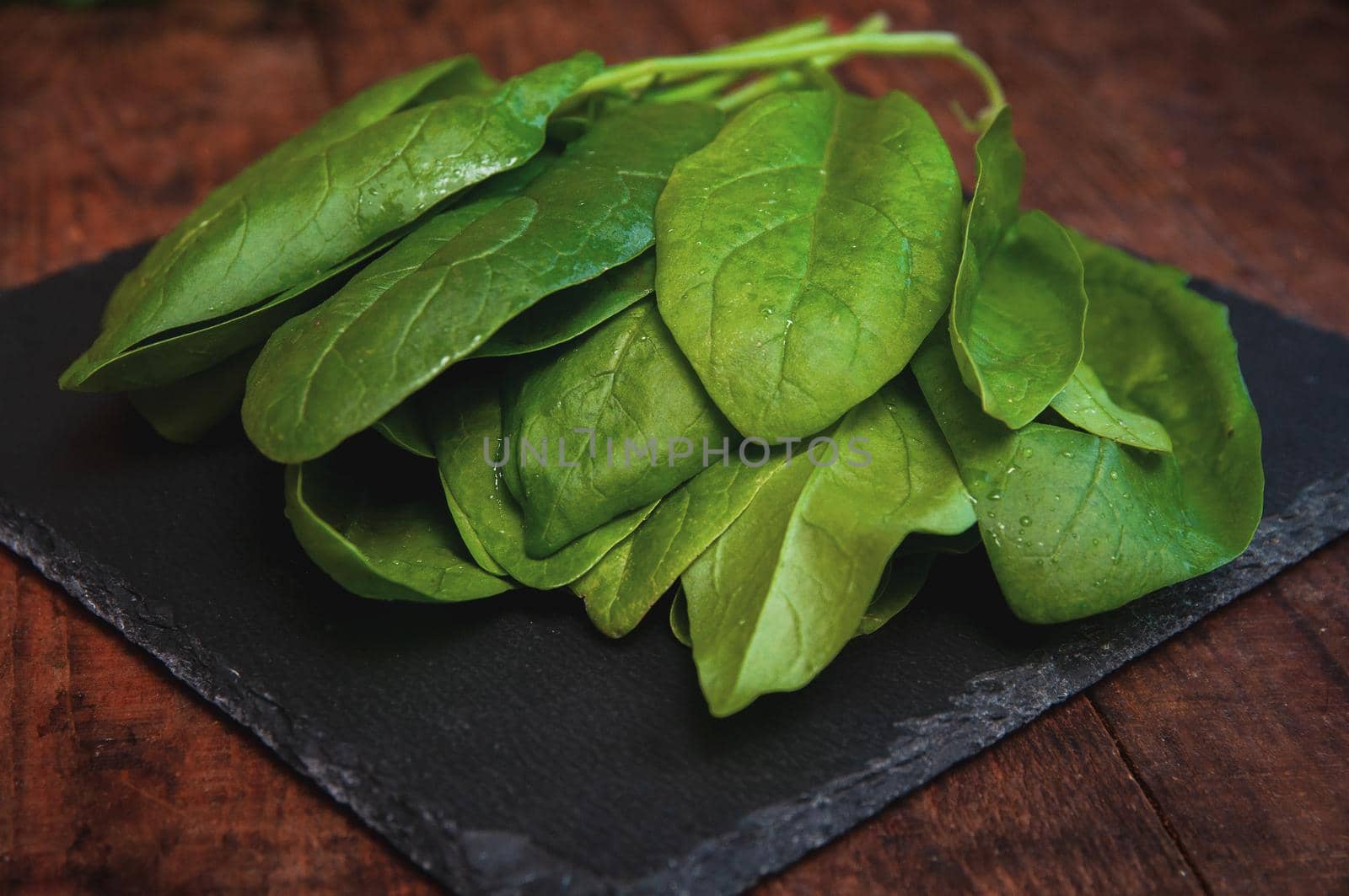 fresh spinach lies on a black presentation board located on a brown wooden table