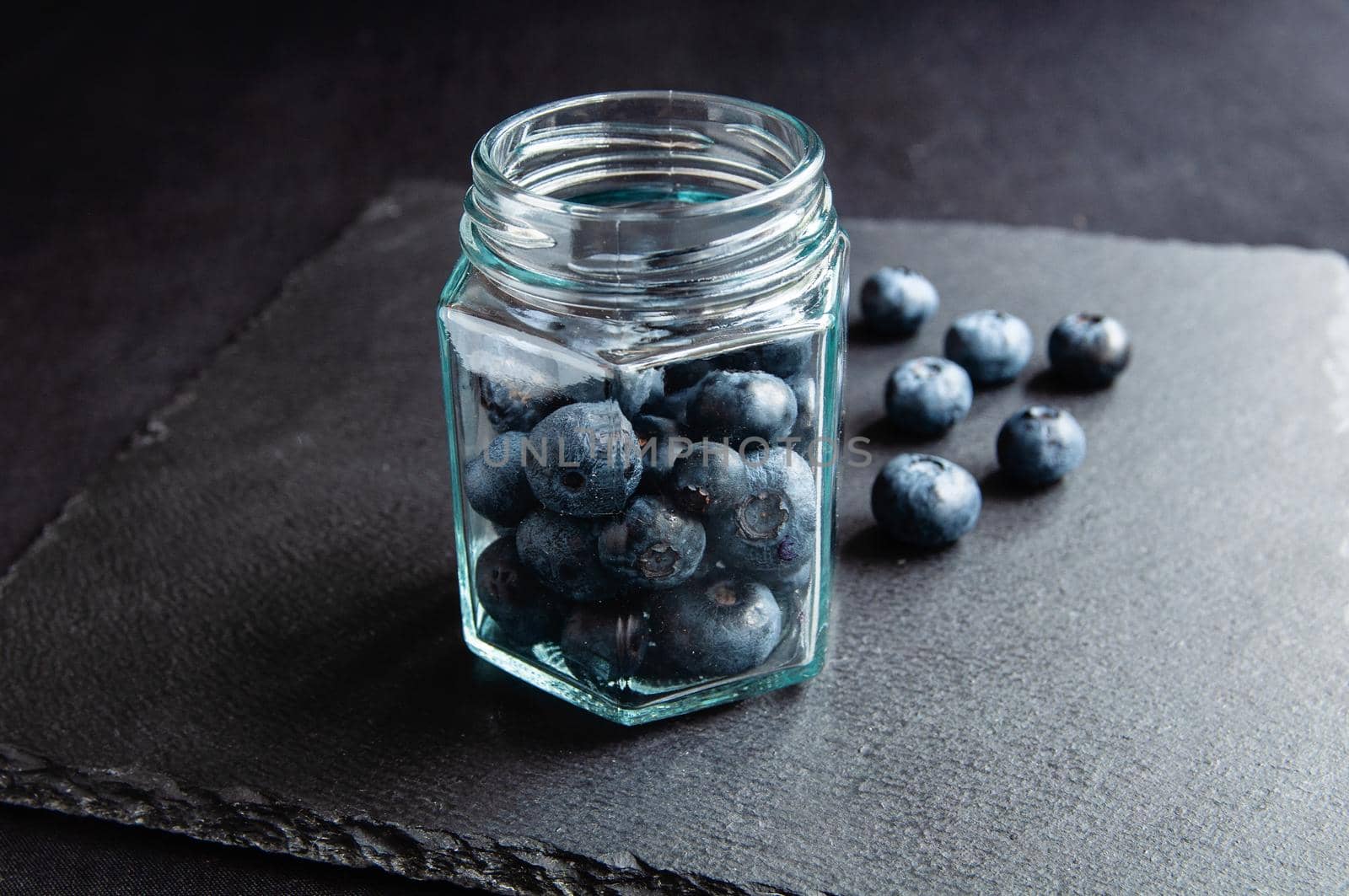 Fresh blueberries in a glass jar and laid out on a black board. by ozornina