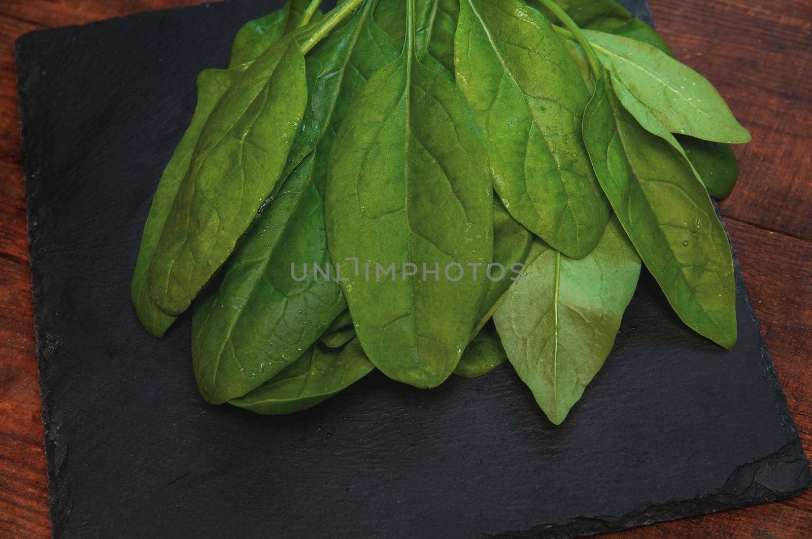 fresh spinach lies on a black presentation board located on a wooden table by ozornina