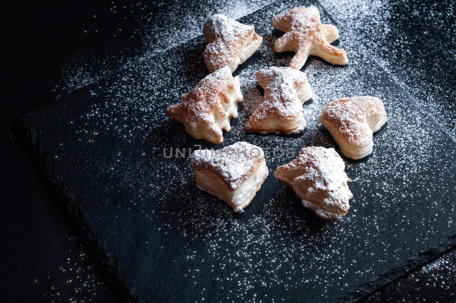 Christmas puff pastry cookies on a black slate background, sprinkled with powdered sugar
