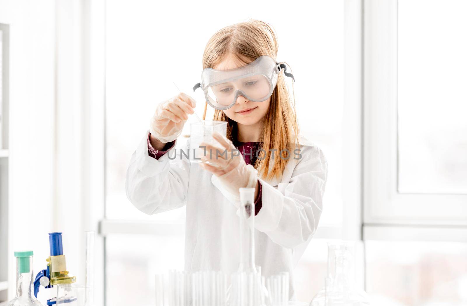 Girl doing scientific chemistry experiment wearing protection glasses. Schoolgirl with equipment and chemical liquids on school lesson