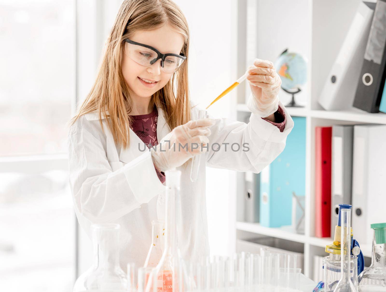 Girl doing scientific chemistry experiment wearing protection glasses and measuring liquid. Schoolgirl with test equipment on school lesson