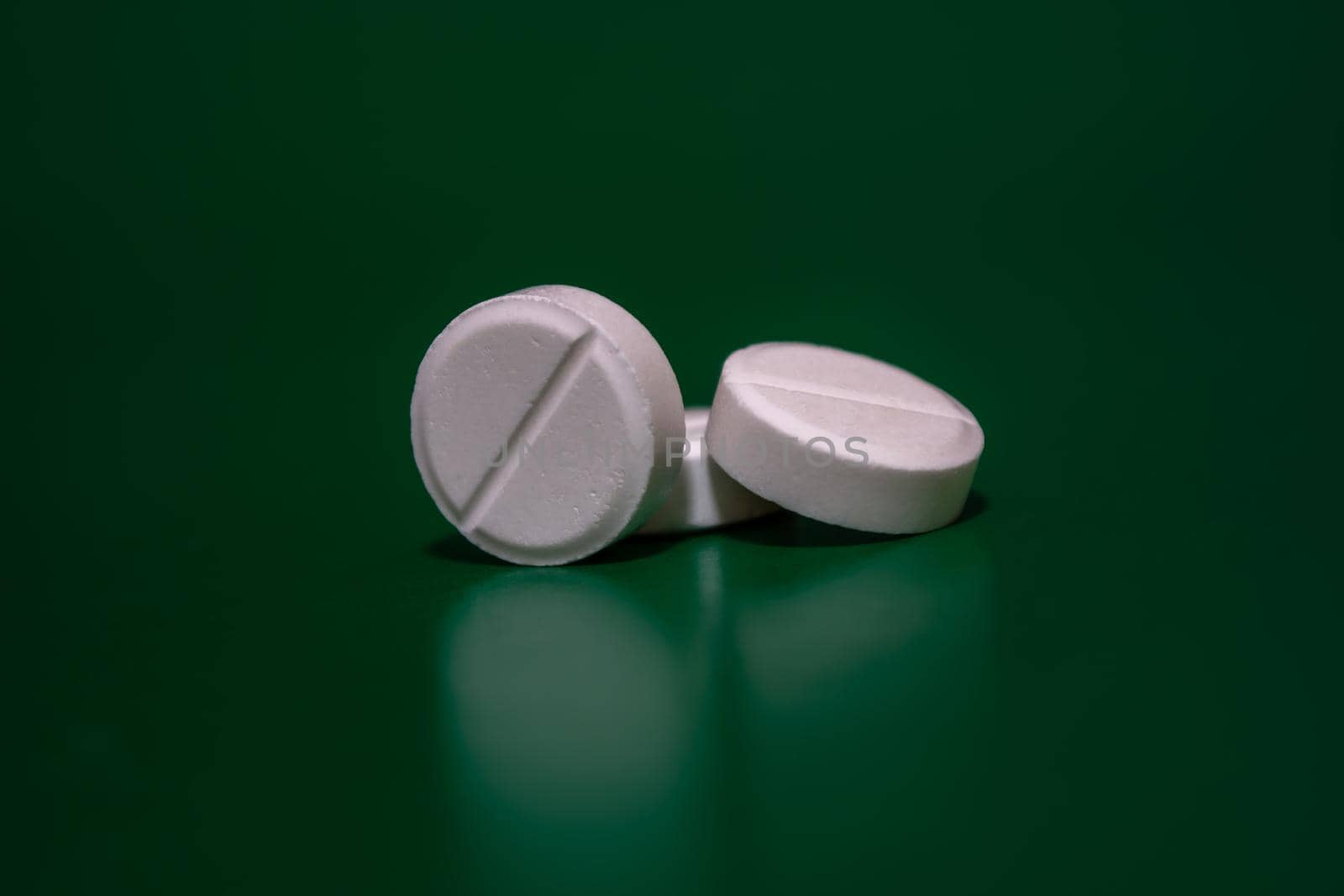 White pills on a green background. Medical theme. Selective focus. Side view of a pile of tablets.