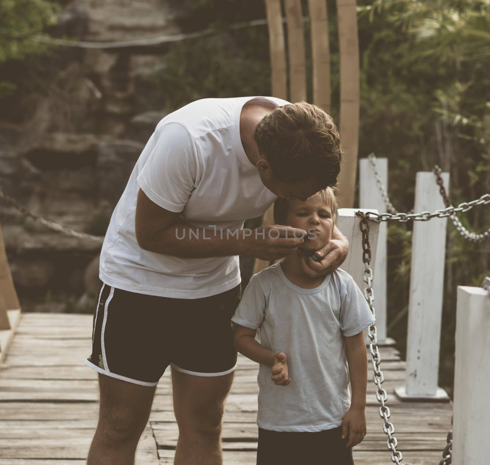 Vintage matte effect photo lifestyle walk moment. Man care treat kid face sore, gesture hand look on boy. Father hug hold child son closely arm embrace, fatherhood love. Family time kindness.