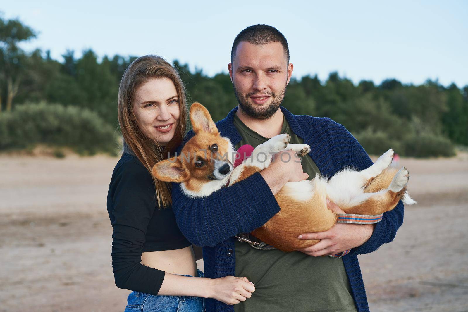 Young happy couple with dog standing on beach. Beautiful girl and guy and Corgi puppy having fun by NataBene
