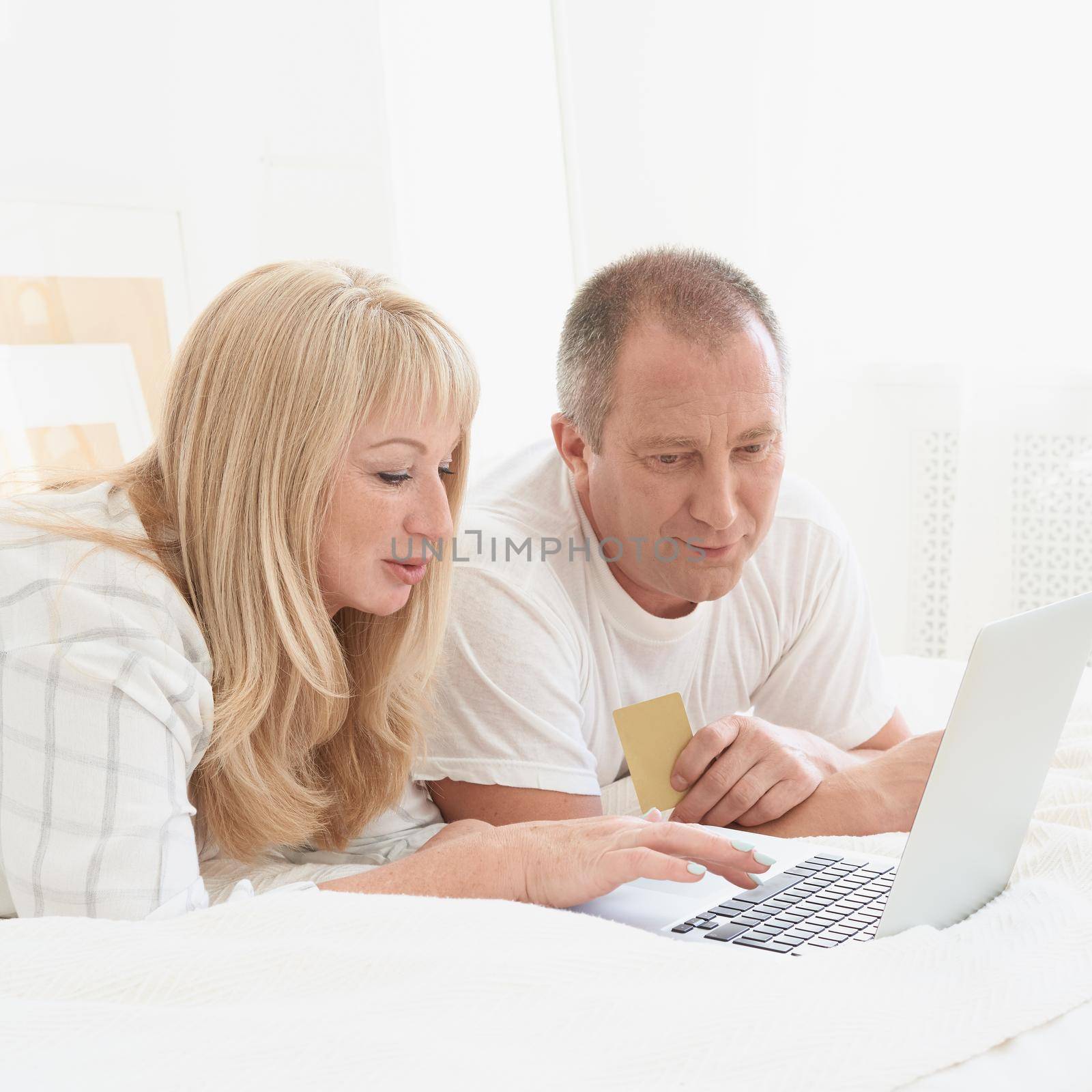 Mature family couple looking at laptop screen. Happy middle aged man holding credit card by NataBene