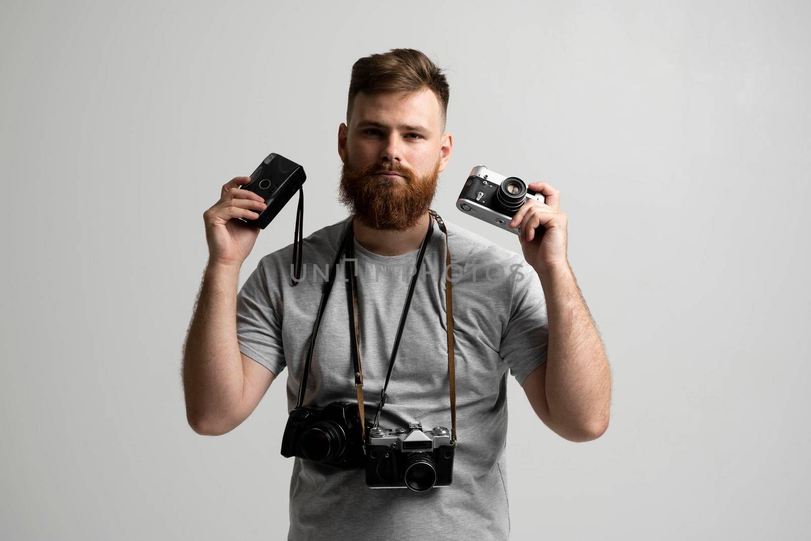 Professional photographer in a grey t-shirt with a bunch of different vintage cameras in a hands and on a shoulder looking on a camera and ready for make a good shoot. by vovsht