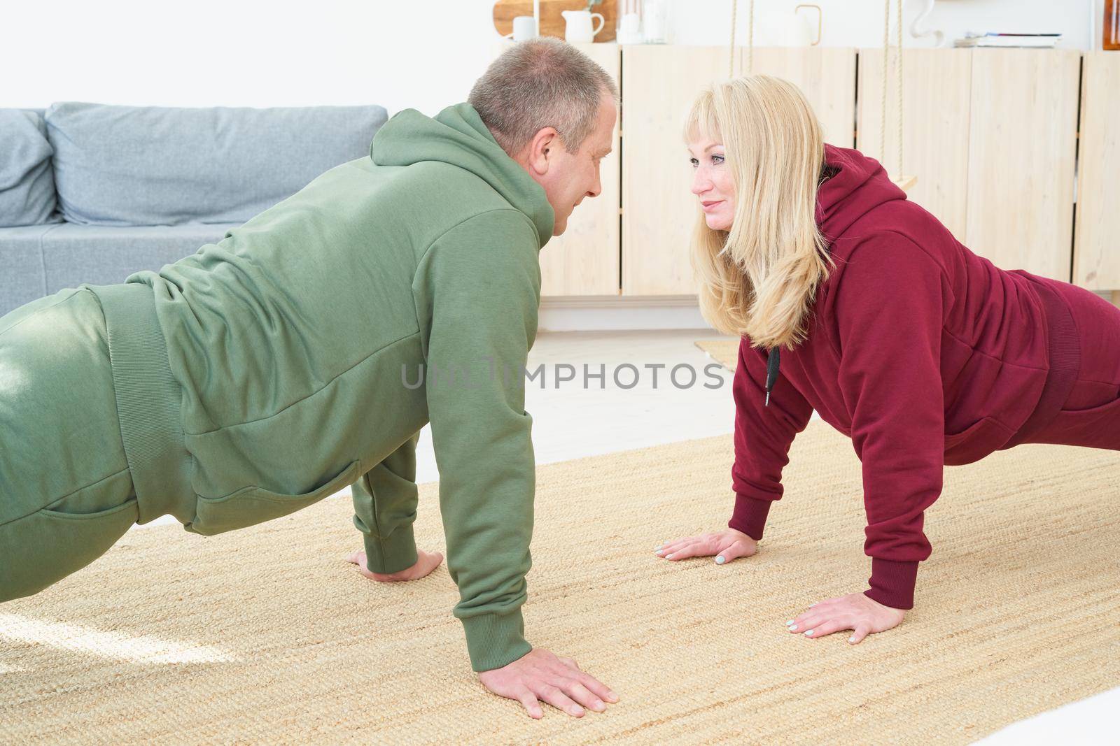 active mature couple doing plank exercise and looking each other in living room at home. Home fitness, activewear.
