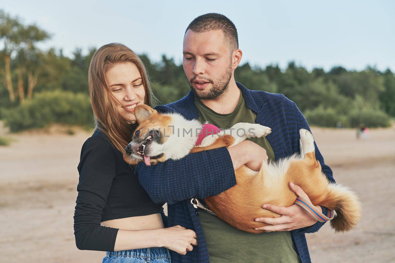 Young happy couple with dog standing on beach. Beautiful girl and guy and Corgi puppy having fun by NataBene