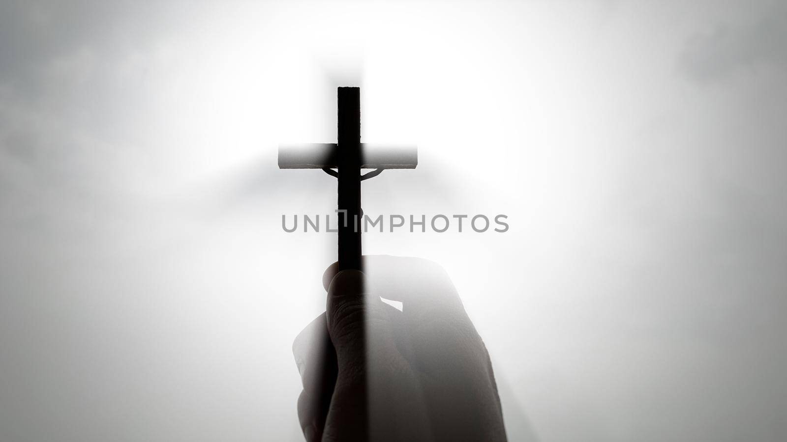 Hand holding Holy Cross with bright sky background.