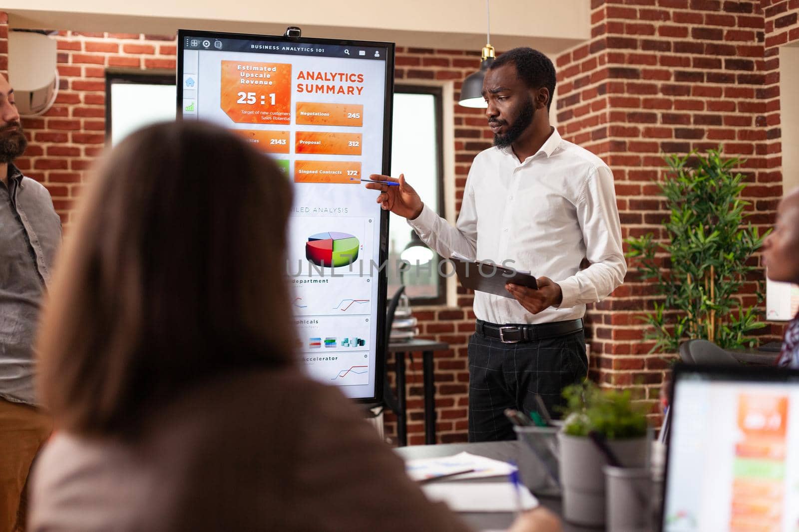 African american businessman showing company graph on monitor discussing management statistics during business meeting in startup office. Diverse businesspeople planning marketing partnership
