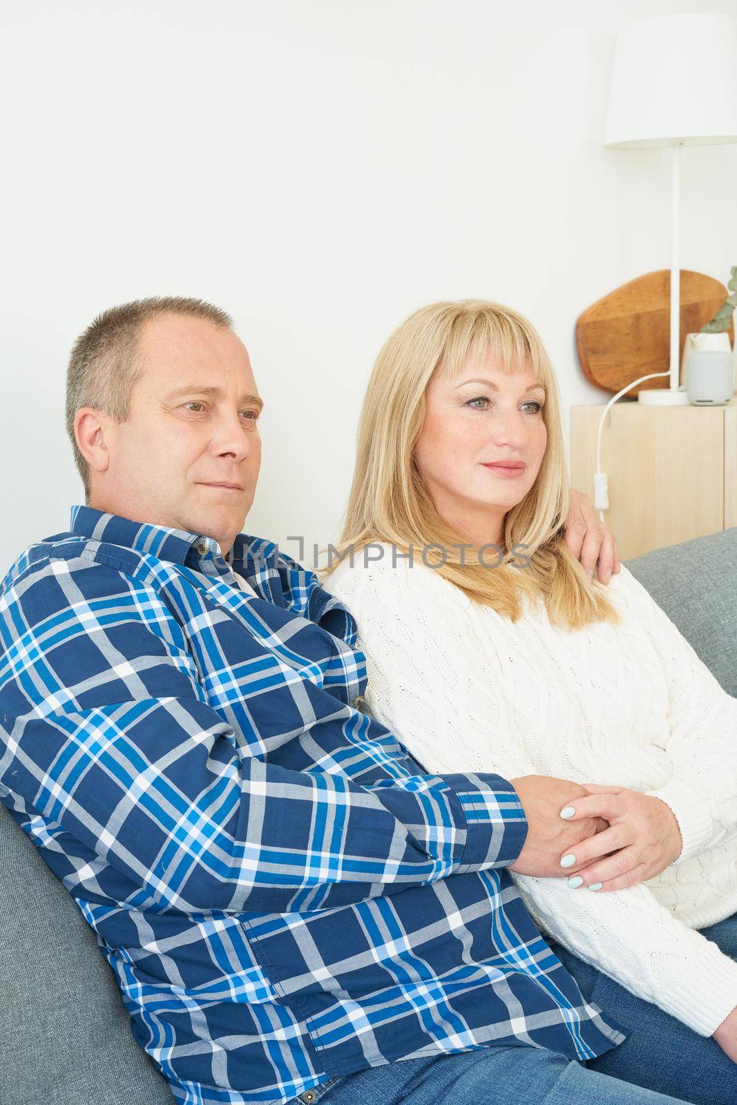 Waist portrait of mature couple in home interior on sofa. Handsome man and attractive middle age woman enjoying spending time together watching movie on TV