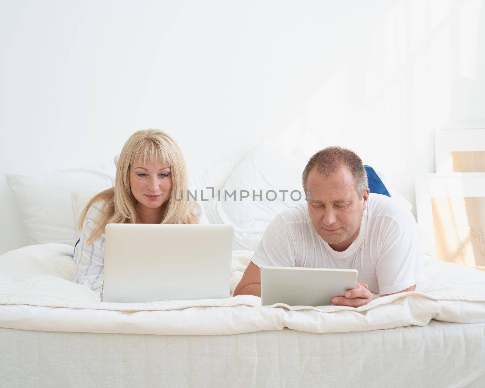 Mature married couple planning travel, choosing vacation, looking for tickets, booking hotel. Handsome man with tablet and attractive middle age woman with laptop spending time together