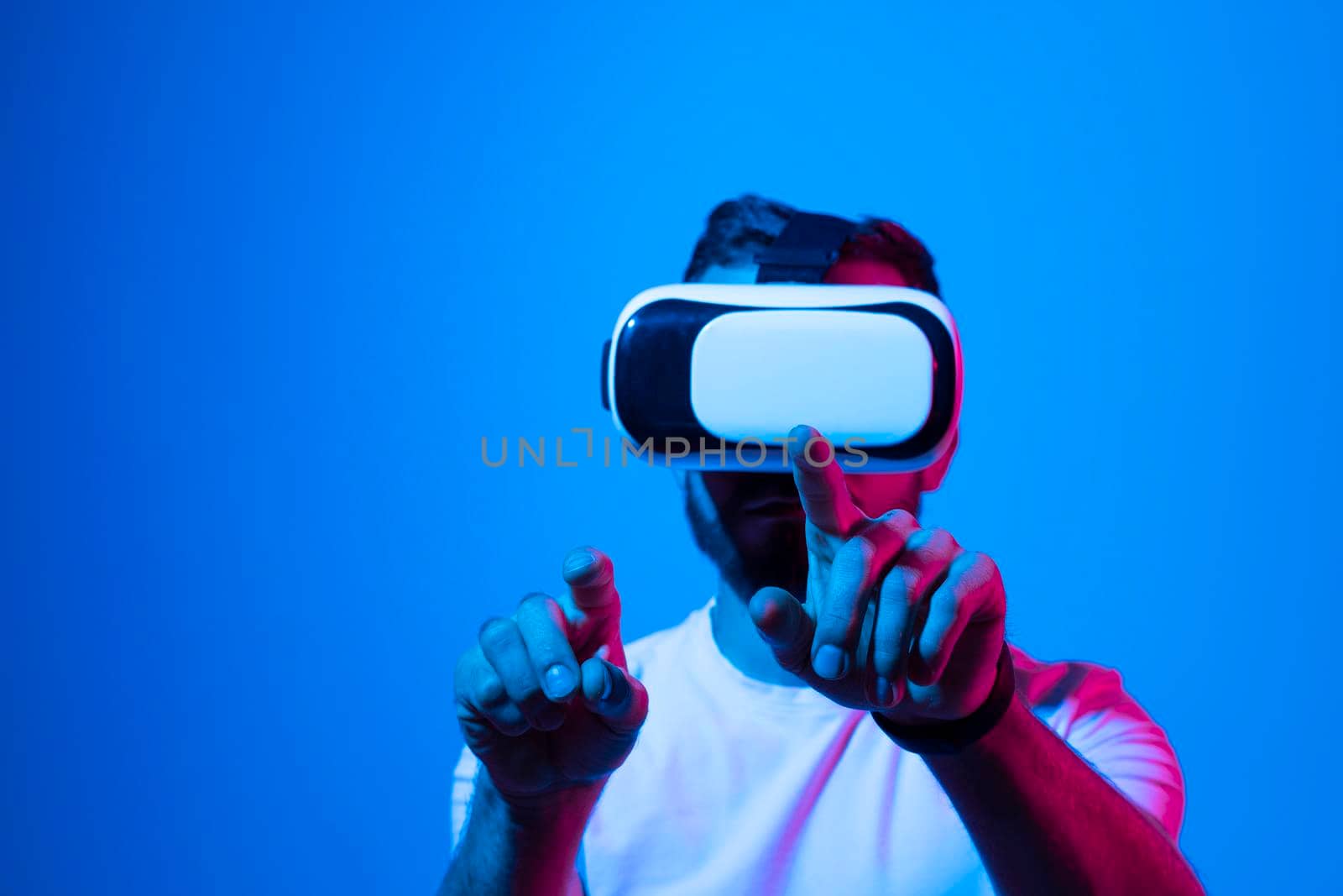 Bearded man playing online VR video game in metaverse with a friends with virtual reality goggles and trying to touch something with both hands. Future technology concept