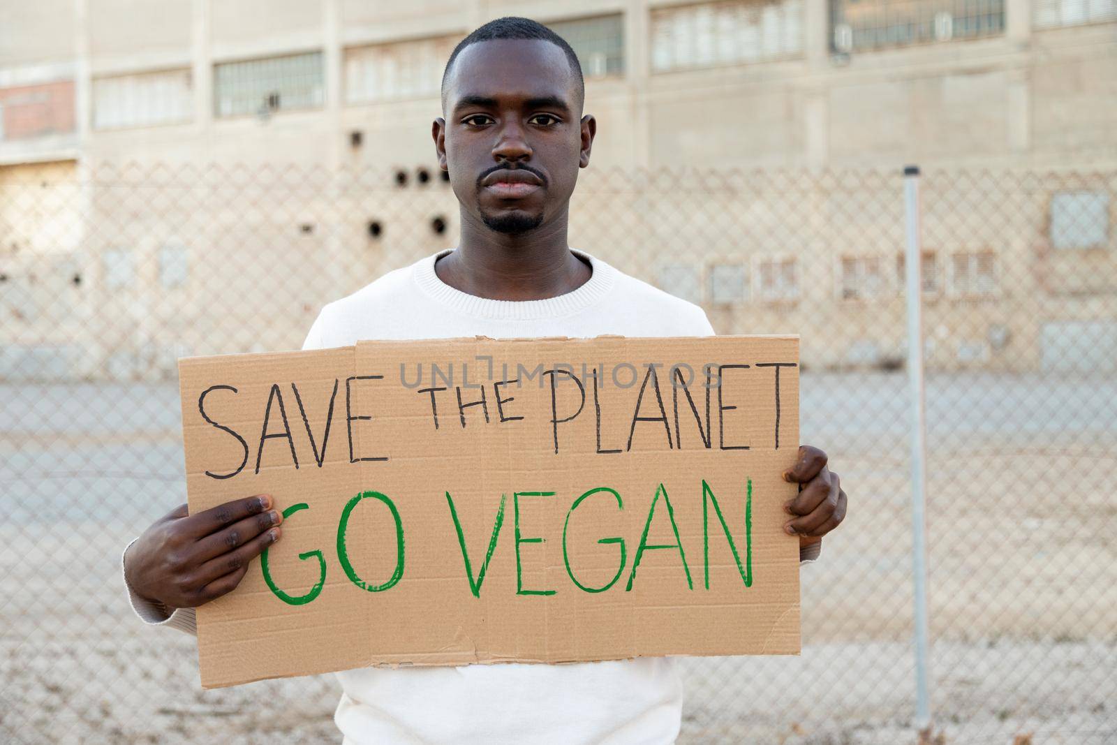 Young African American man looking at camera holding cardboard sign Save the planet, go vegan by Hoverstock