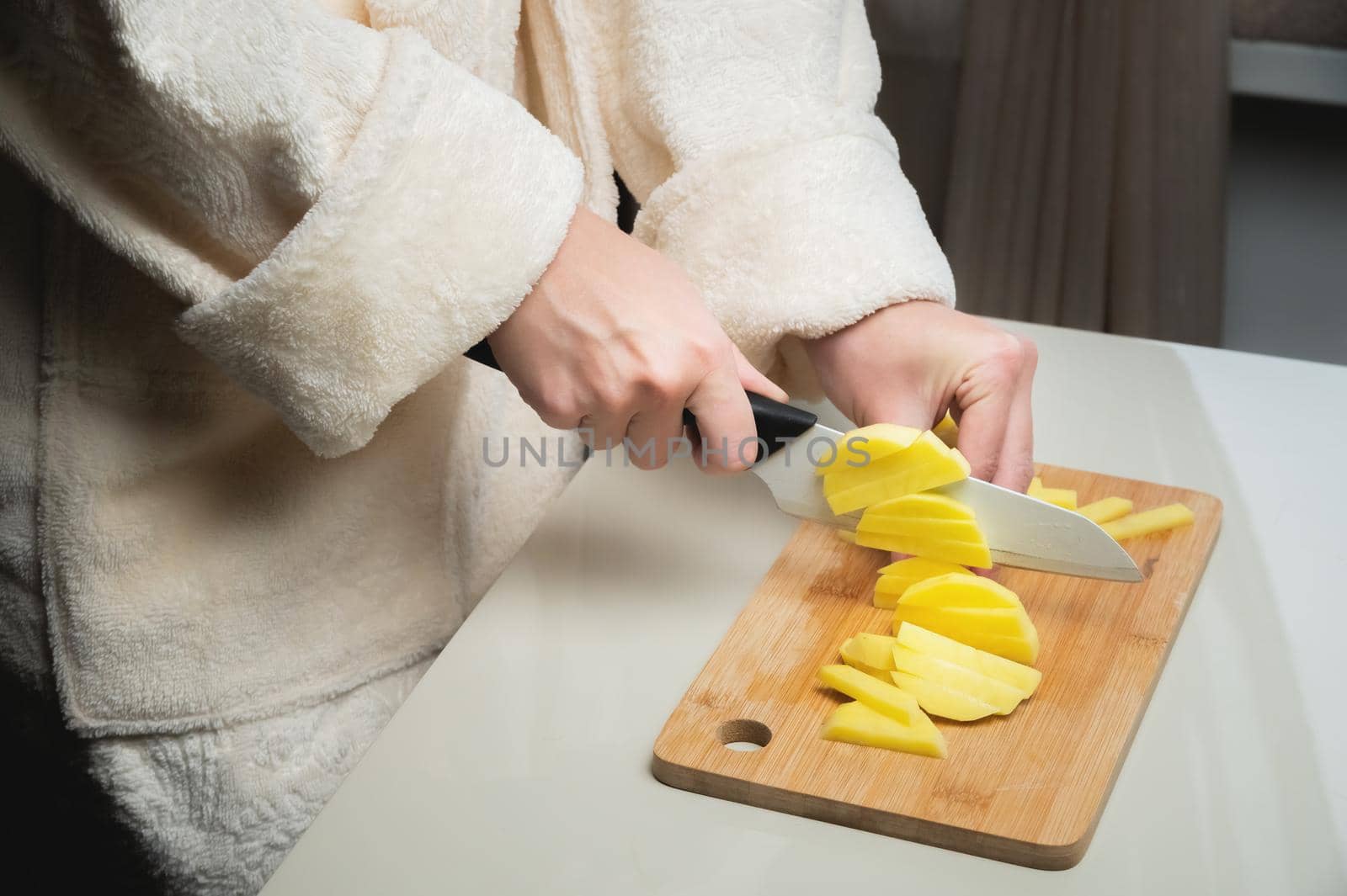 young caucasian woman in a bathrobe stands and cuts potatoes on a cutting board by yanik88