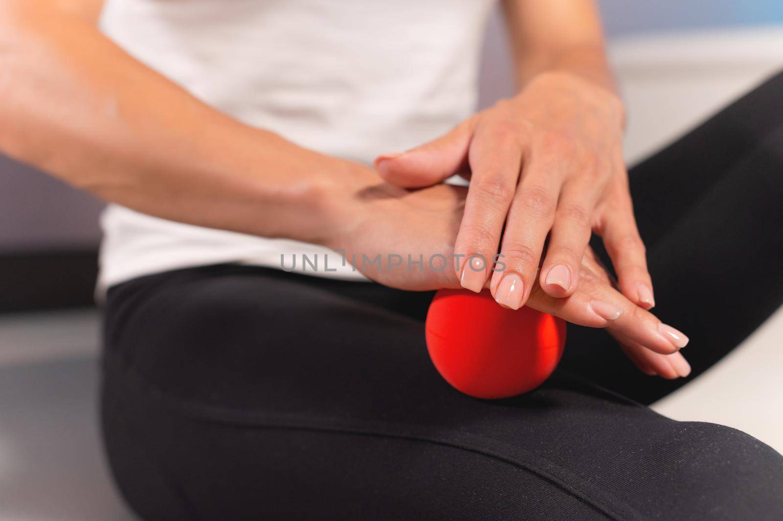 Close-up of a caucasian woman giving herself a myofascial thigh massage with a massage red ball.