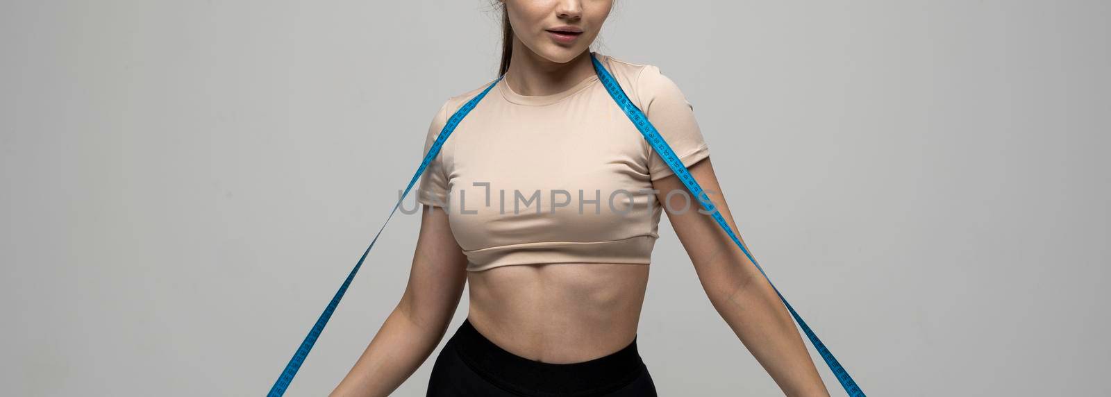 Sport fitness attractive young brunette girl in sportswear with blue measuring tape on her shoulder on white background Sports and diets