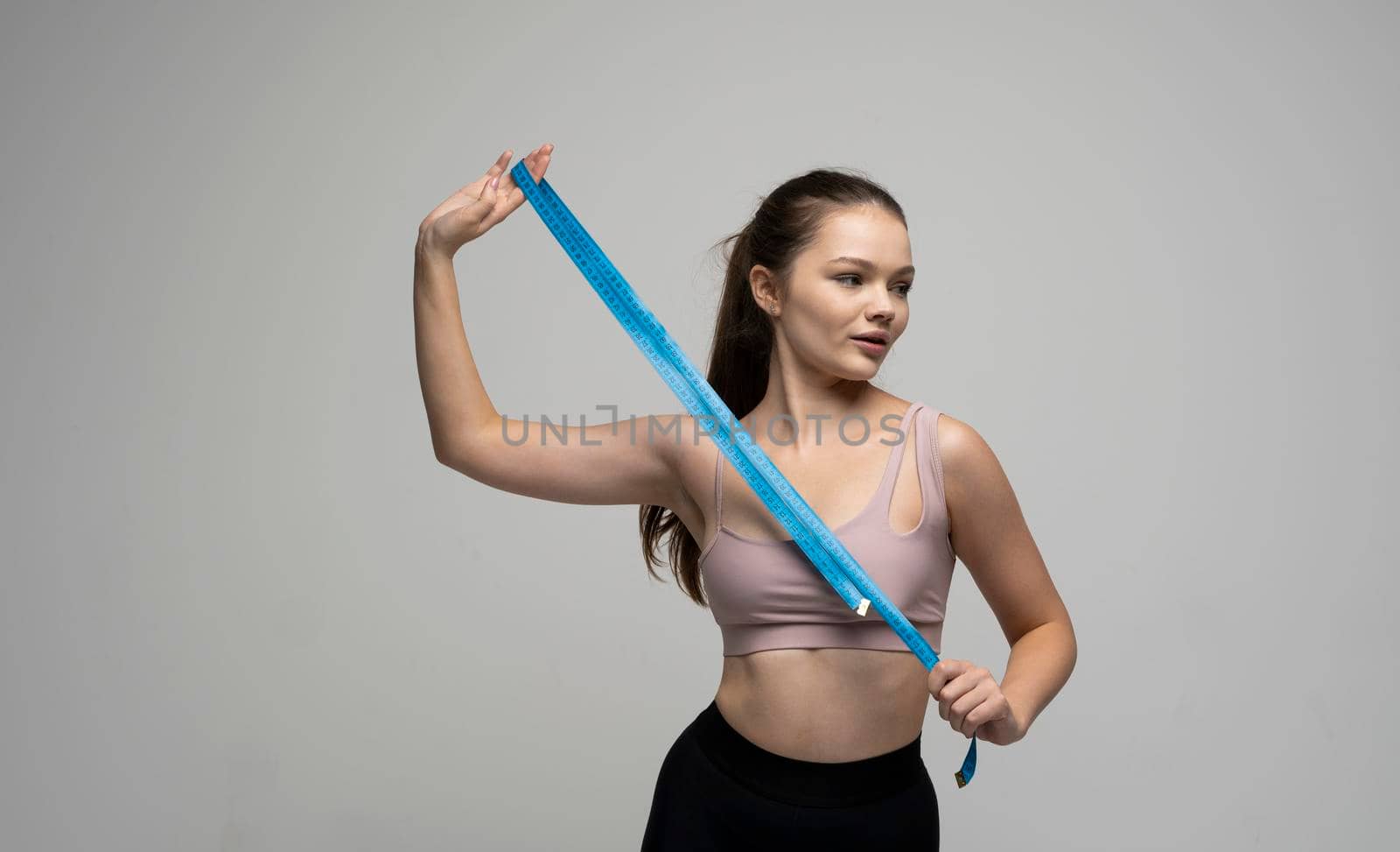 Beautiful attractive sporty slim brunette woman in beige top with blue measuring tape on white background