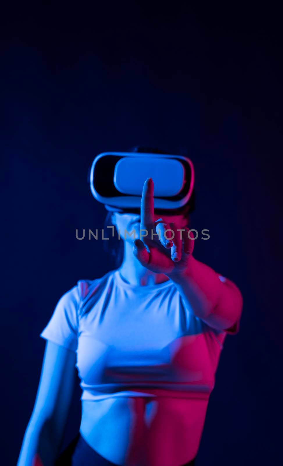Modern architect using virtual reality glasses at workplace and touch something in virtual world. Woman working in VR goggles in neon light. Designer working in VR studio. by vovsht