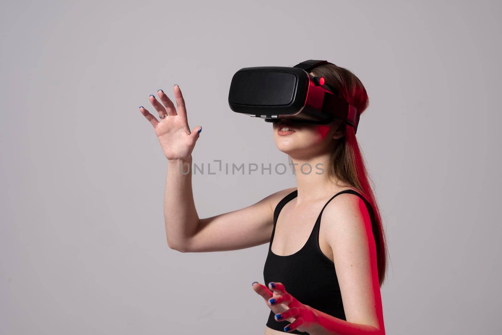 Woman using virtual reality glasses in a studio with a neon light. Business woman wearing VR goggles and interacts with cyberspace using swipe and stretching gestures