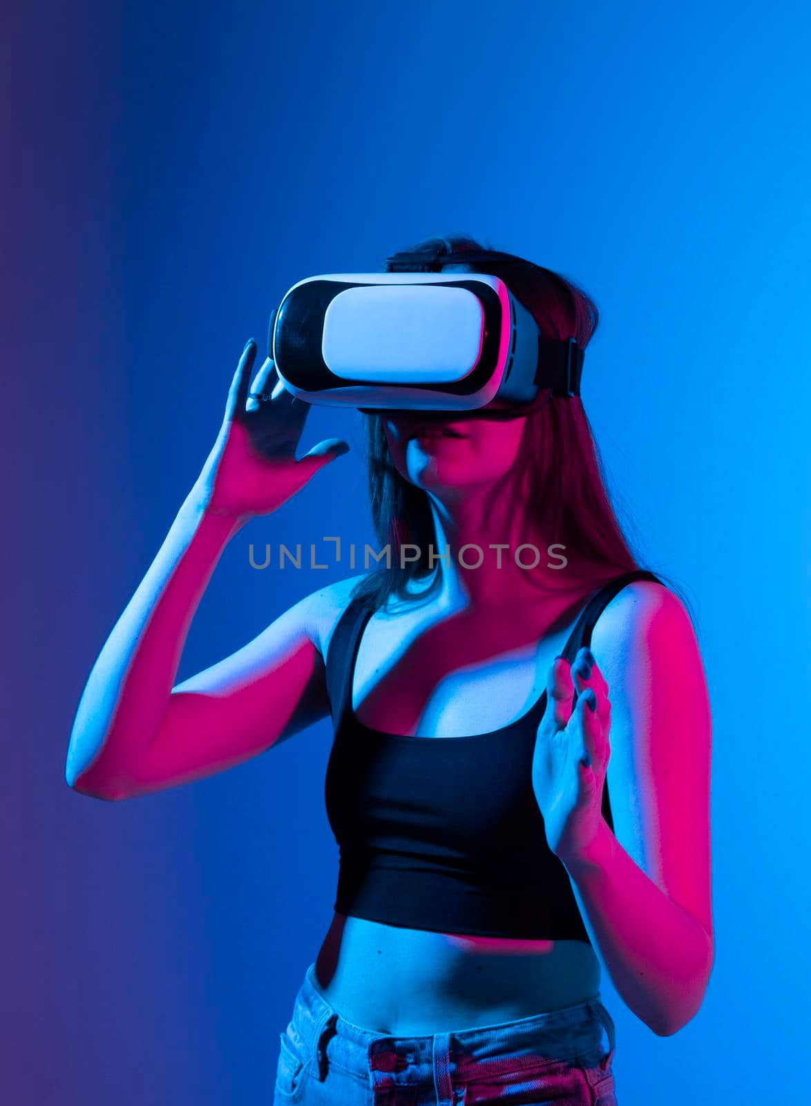 Young woman using VR headset helmet and interacts with a friends in metaverse social network using swipe and stretching gestures. She watching virtual reality 3d video with a friends