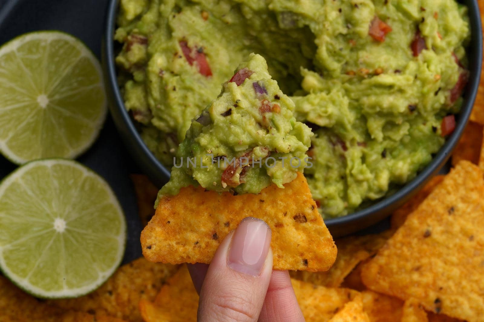 Top view of hand with tasty tortilla chips or nachos homemadewith fresh homemade guacamole dip sauce. High quality photo