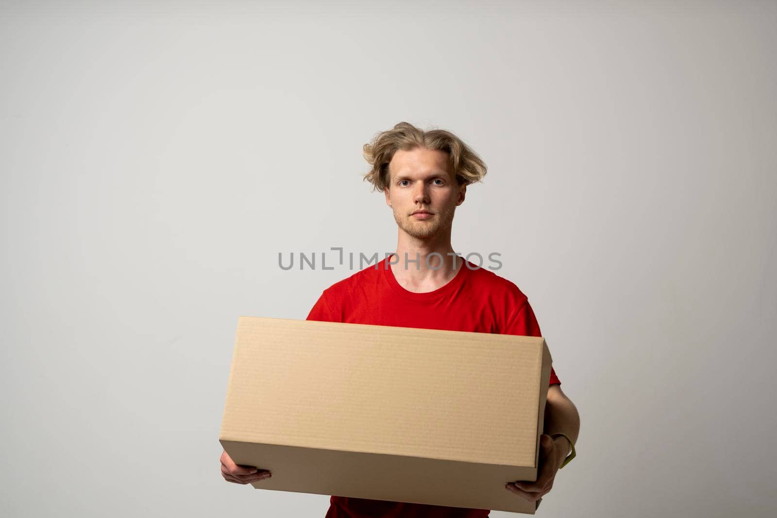 Delivery service. Happy young delivery man in red t-shirt standing with parcel isolated on white background