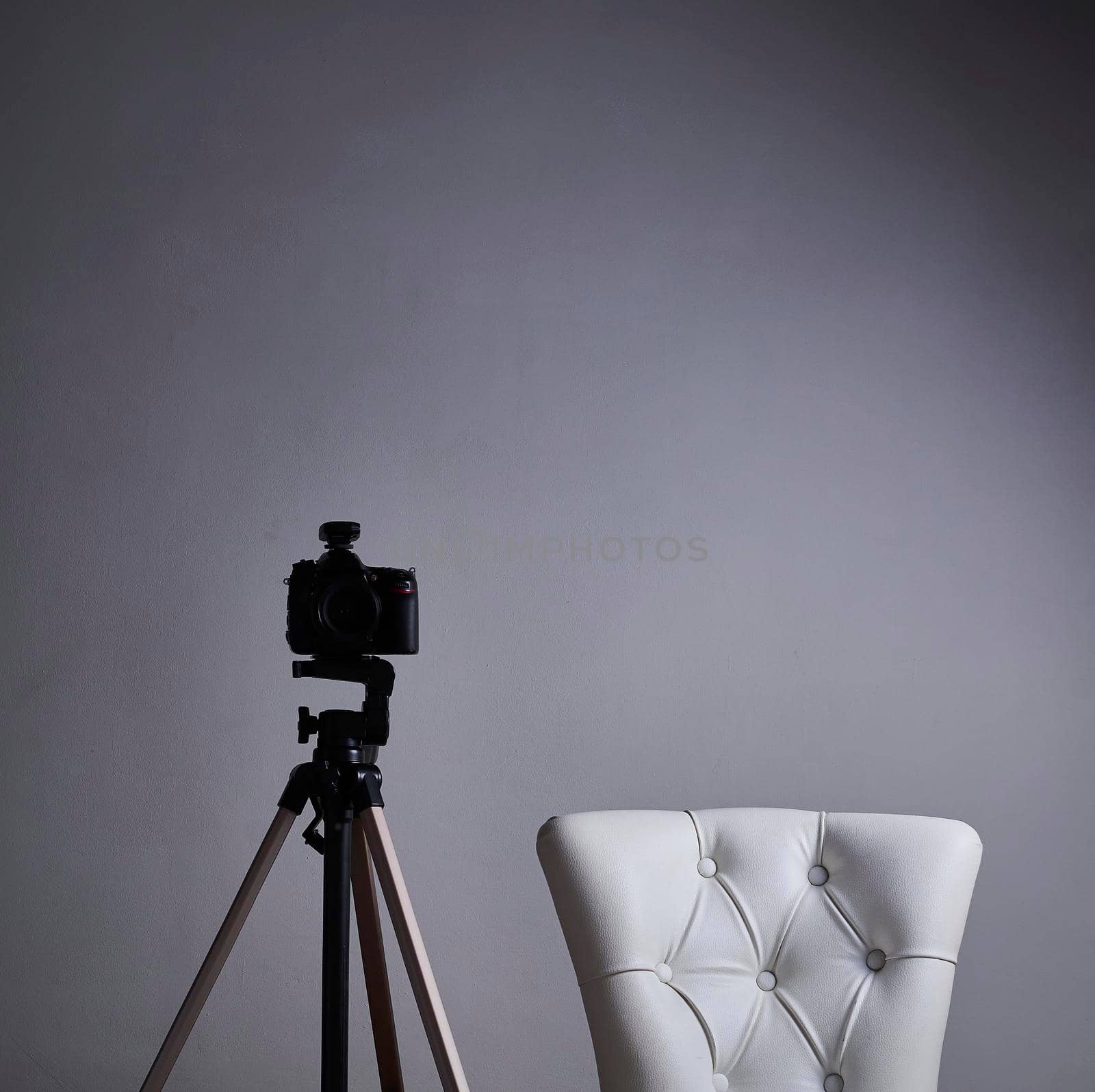 Camera on tripod with white antique armchair, Solitaire, front view and grey background.