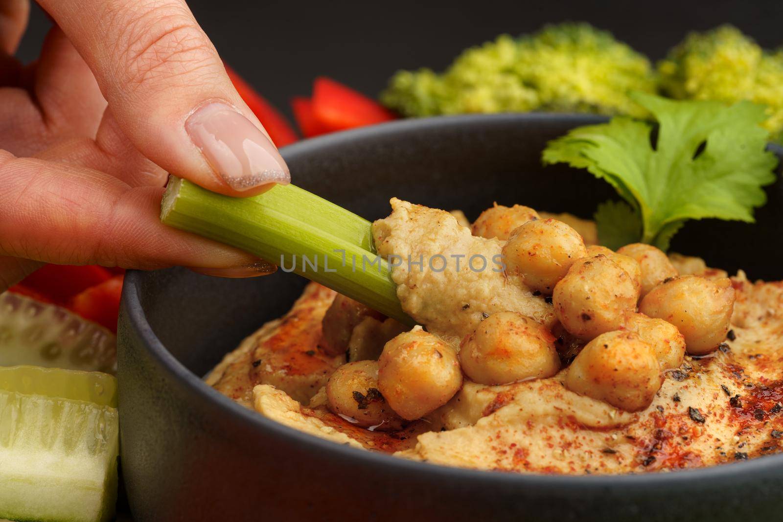 Closeup of hand with celery stick with chickpeas hummus. Tasty hummus with vegetables and smoked paprika by DariaKulkova