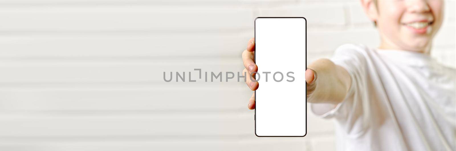 Happy smiling boy showing smartphone mockup in a white backdrop. blank cellphone screen by PhotoTime