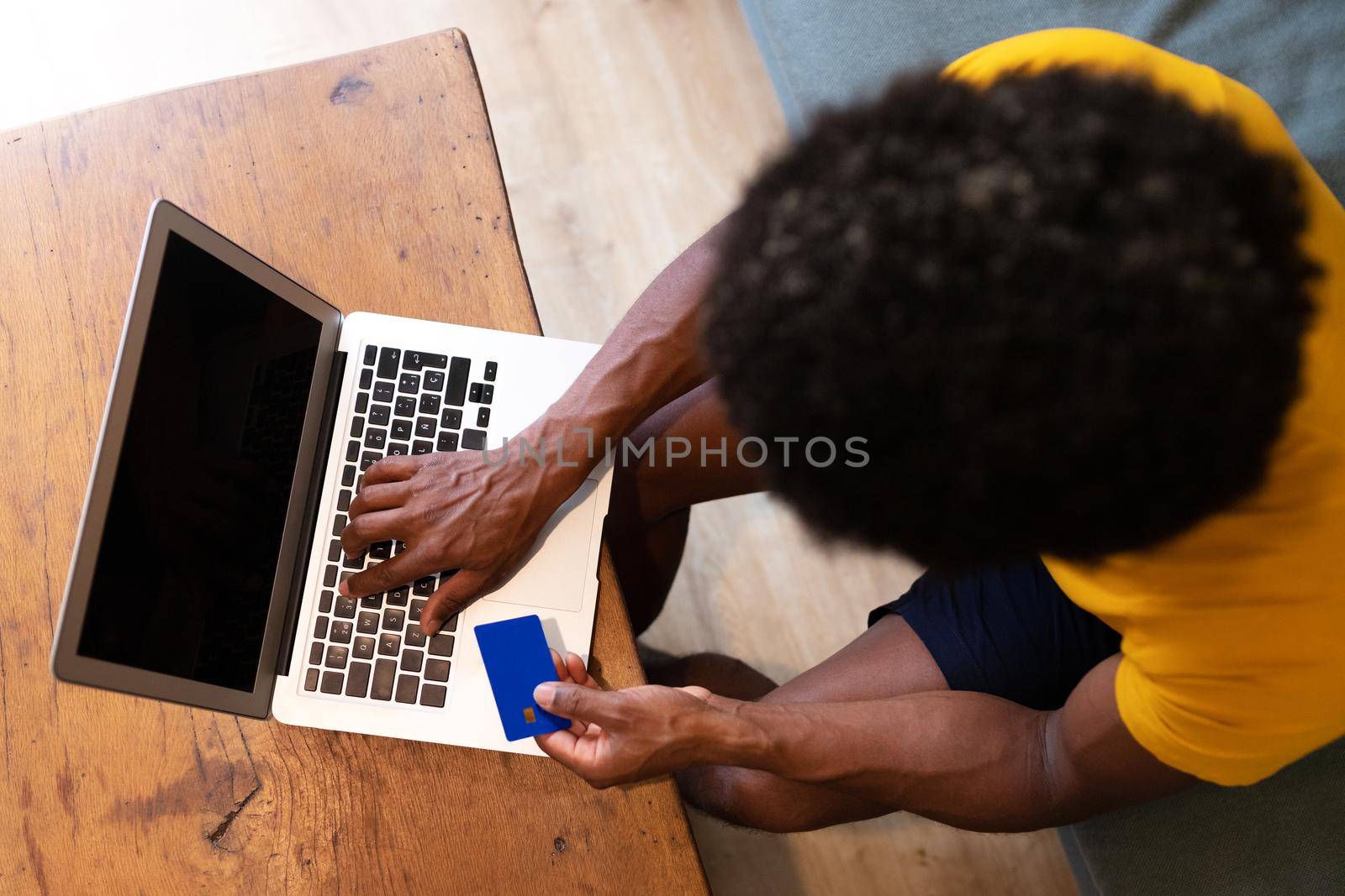 Top view African American man buying things online with laptop and credit card. by Hoverstock