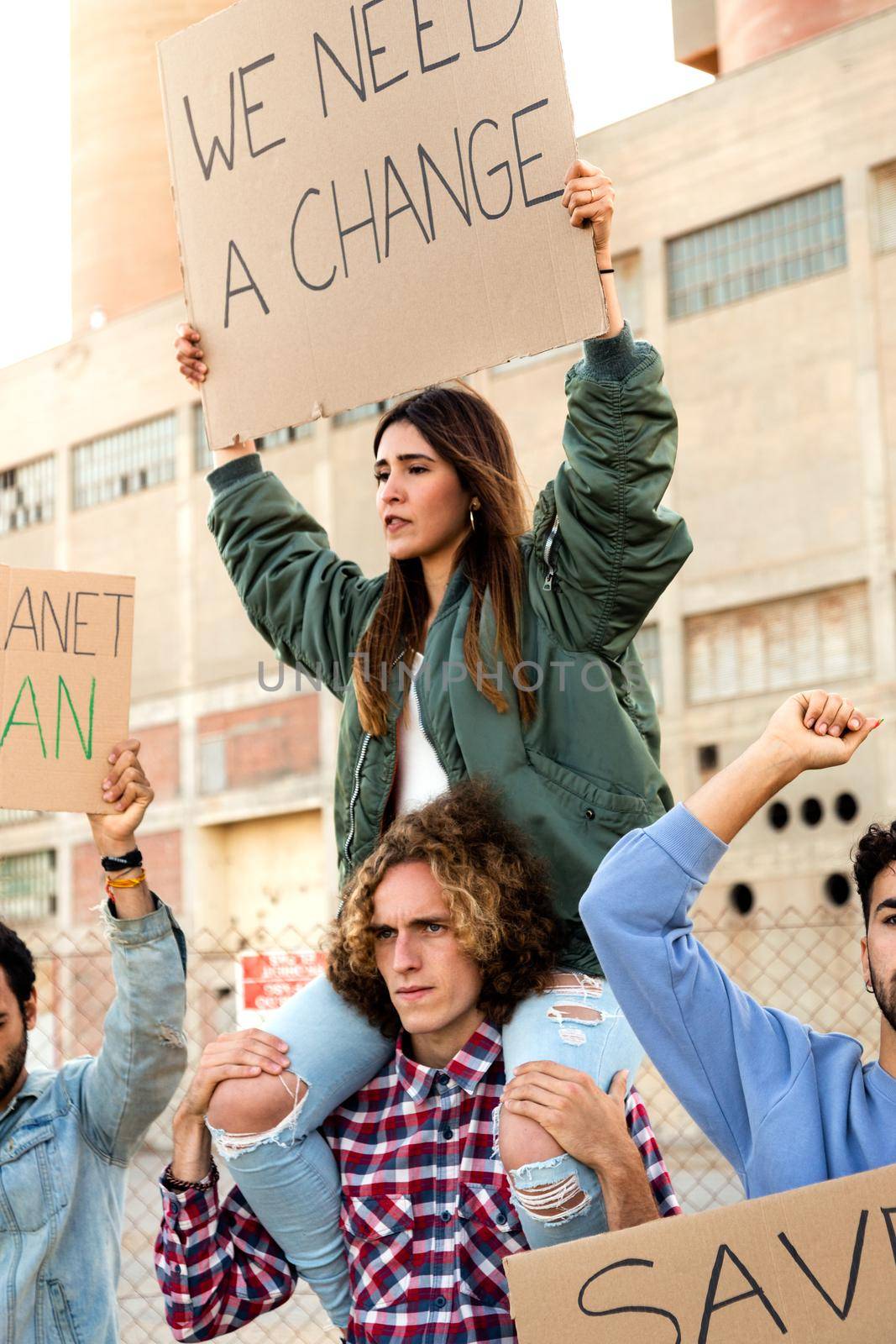 Young hispanic woman sitting on mans shoulder protesting against climate change in demonstration. Vertical image. by Hoverstock