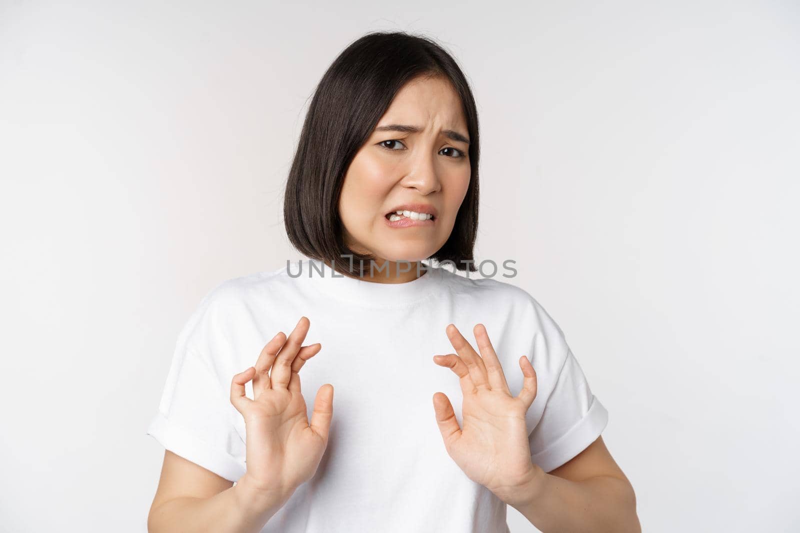 Disgusted asian woman rejecting smth, grimacing from dislike and aversion, stare with cringe, refusing offer, standing over white background.