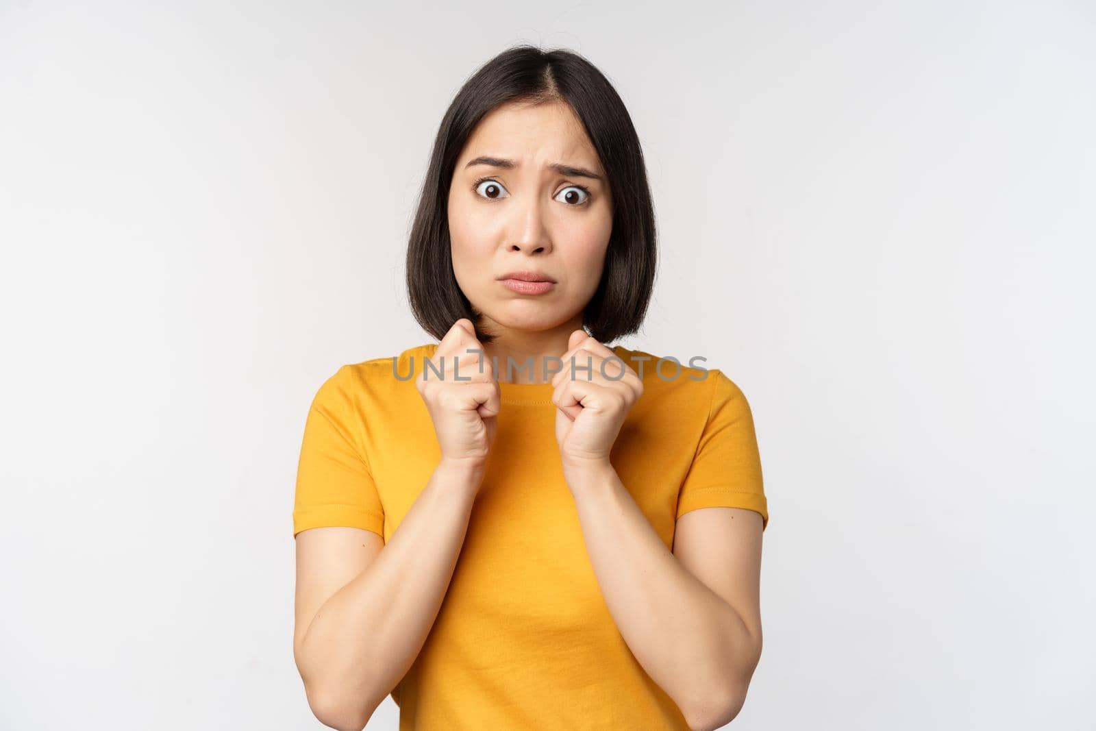 Portrait of scared asian woman shaking from fear, looking terrified and concerned, standing anxious against white background.
