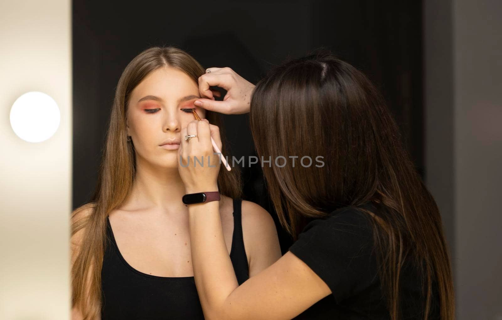 Makeup artist applies eye shadow on a beautiful woman face. Hand of visagiste, painting cosmetics of young beauty model girl. Make up in process. by vovsht