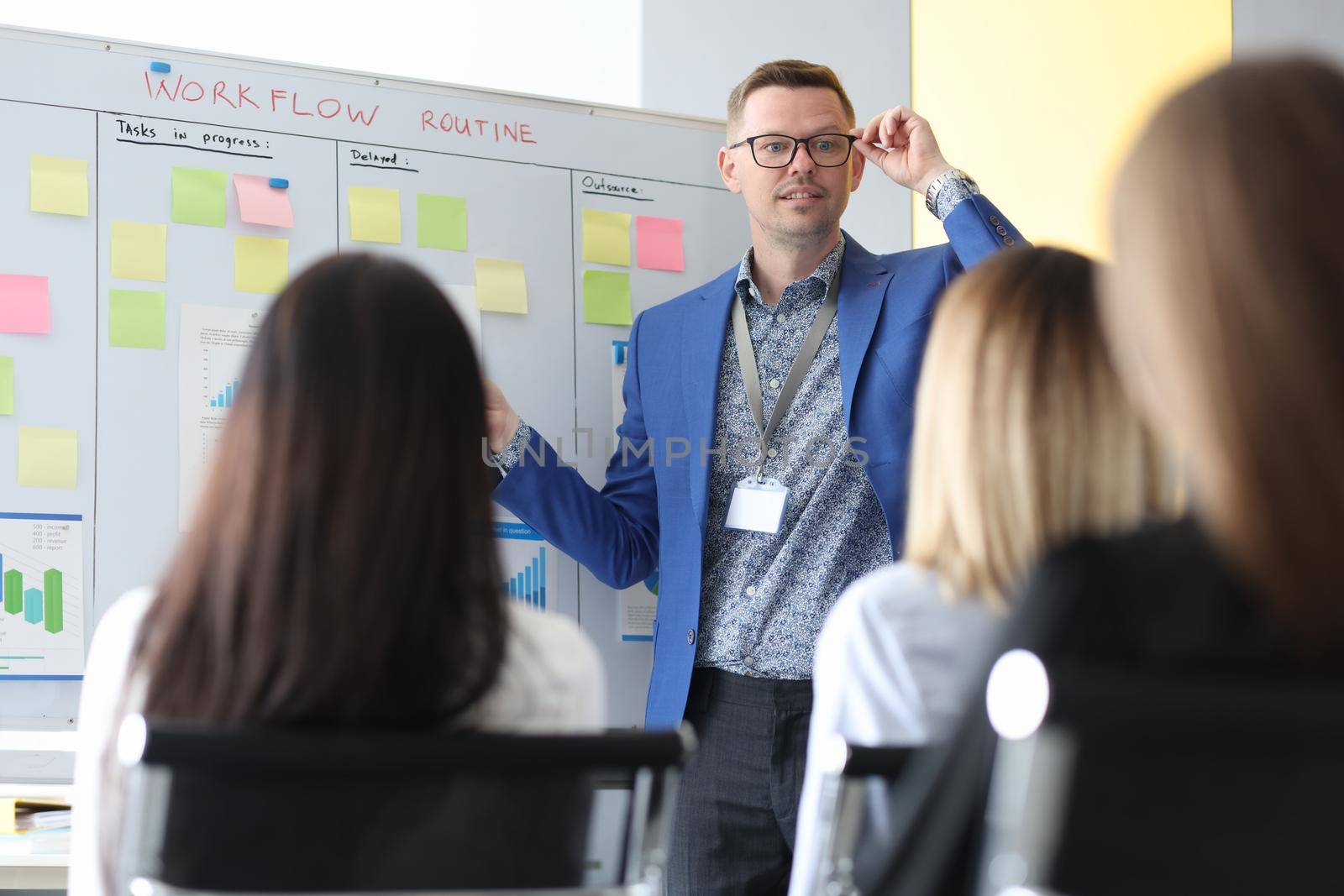 The coach in the office standing at the blackboard teaches women, close-up, blurry. Workspace, goals and motivation