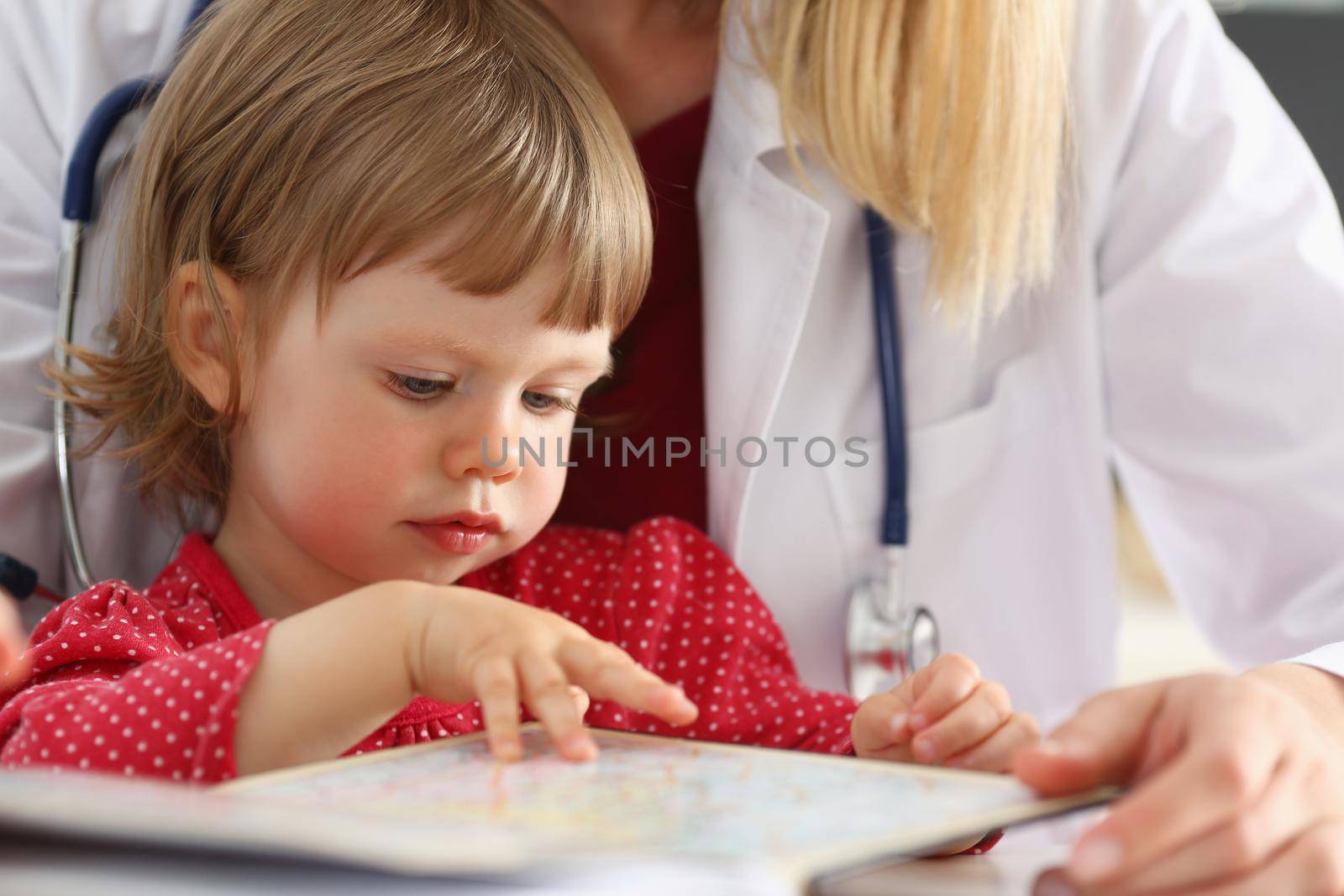 Female pediatrician next to a little girl in a red dress, close-up. Doctor's consultation, intelligence test