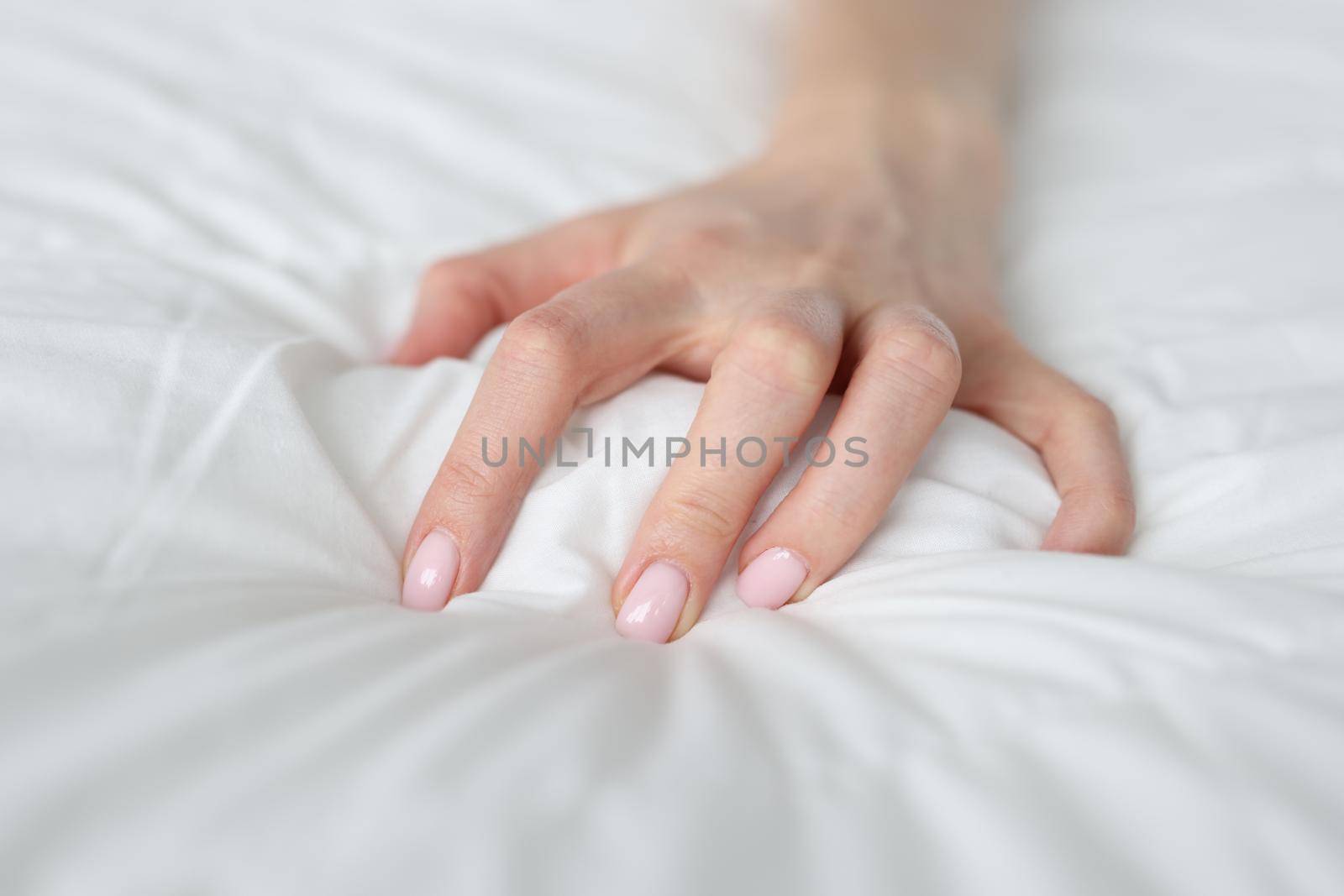 A woman's hand is squeezing a white blanket on the bed, close-up. Pain during sleep, a dangerous health condition