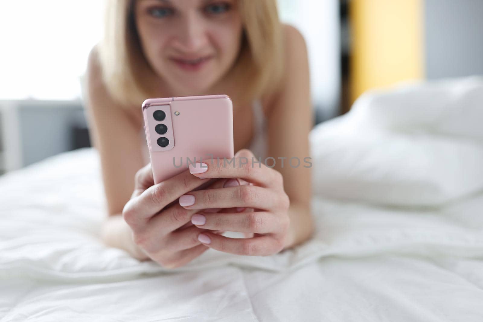 Happy blonde woman lies on the bed with a smartphone by kuprevich