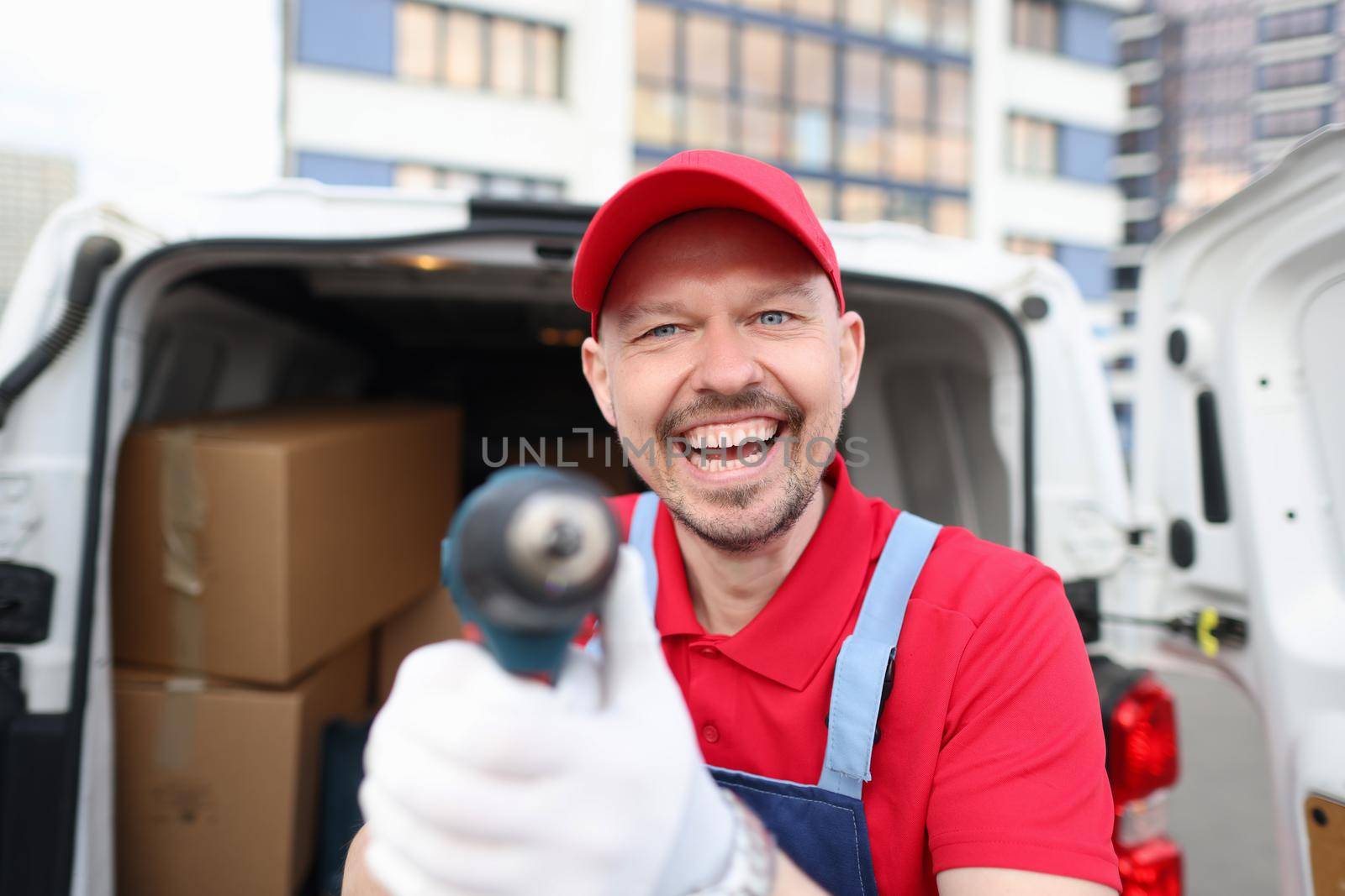 Happy courier in a red uniform shows a tool near a covered van by kuprevich