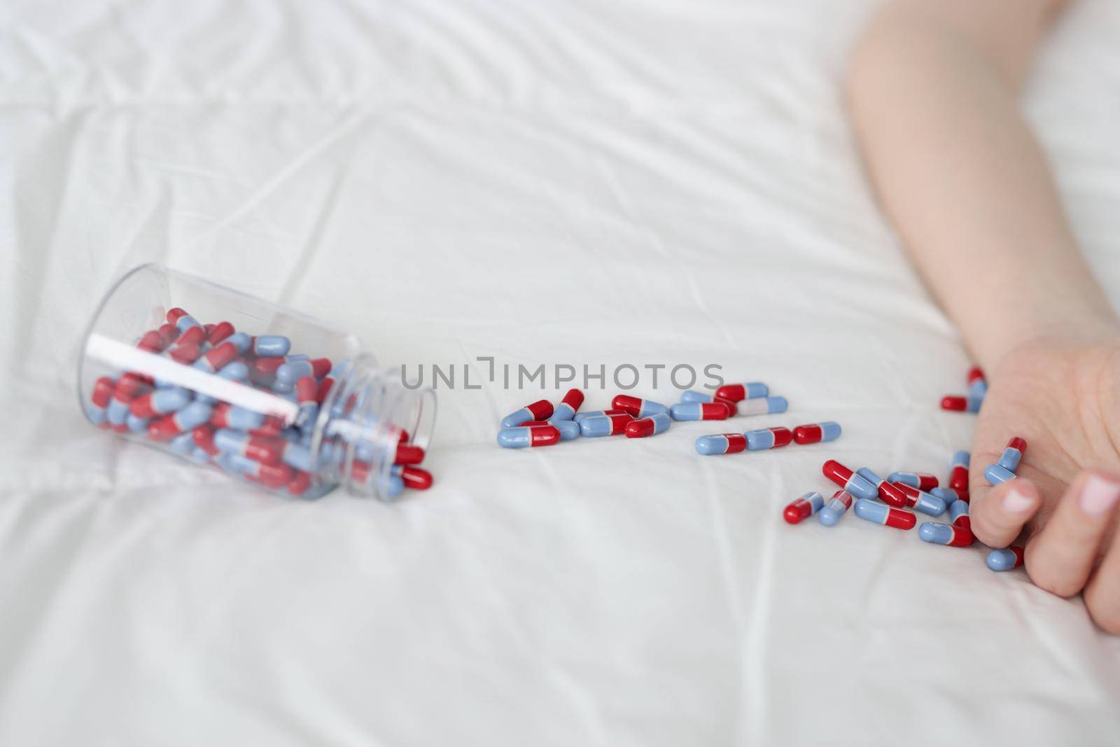 Blue red capsules are scattered on the bed, close-up. Woman poisoned by antidepressants, drug overdose