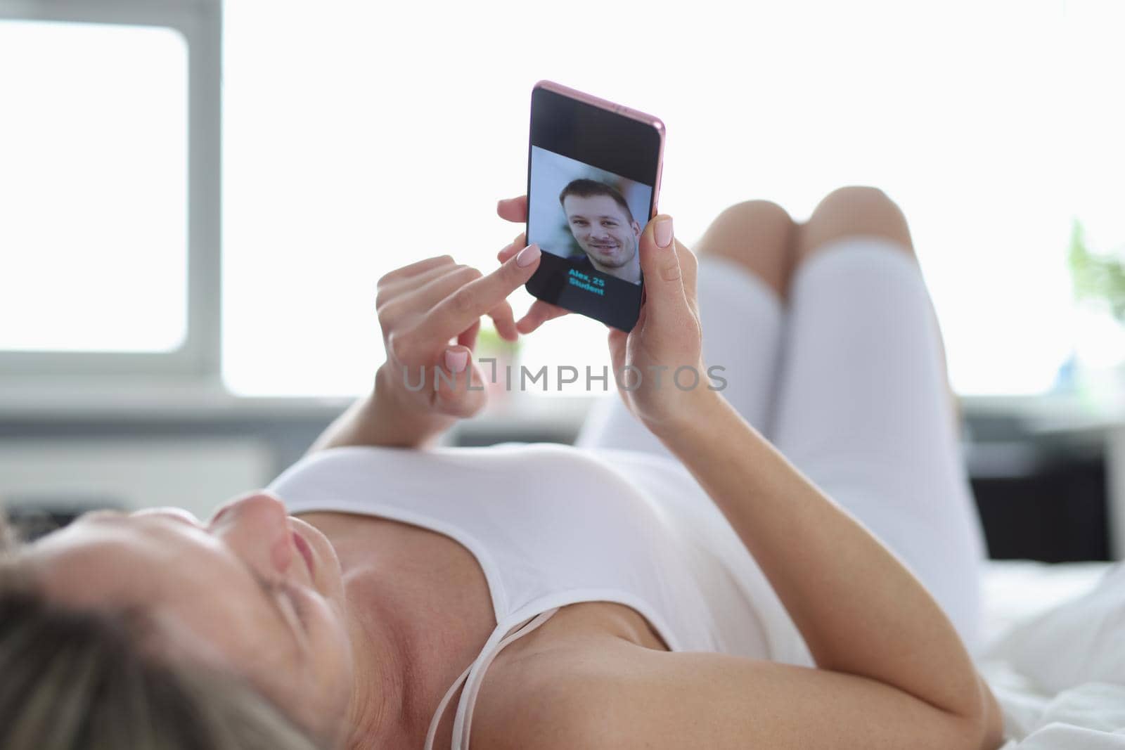 A woman lies on her back on the bed and looks into the phone, close-up. Dating site, search for a marriage partner online