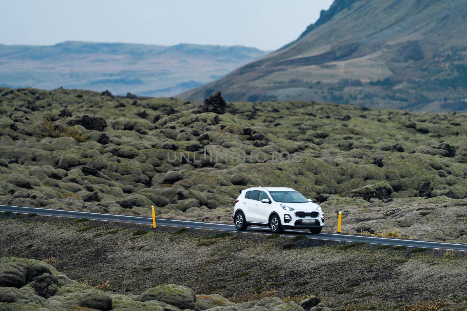 White car driving through huge lava fields covered by moss in Iceland