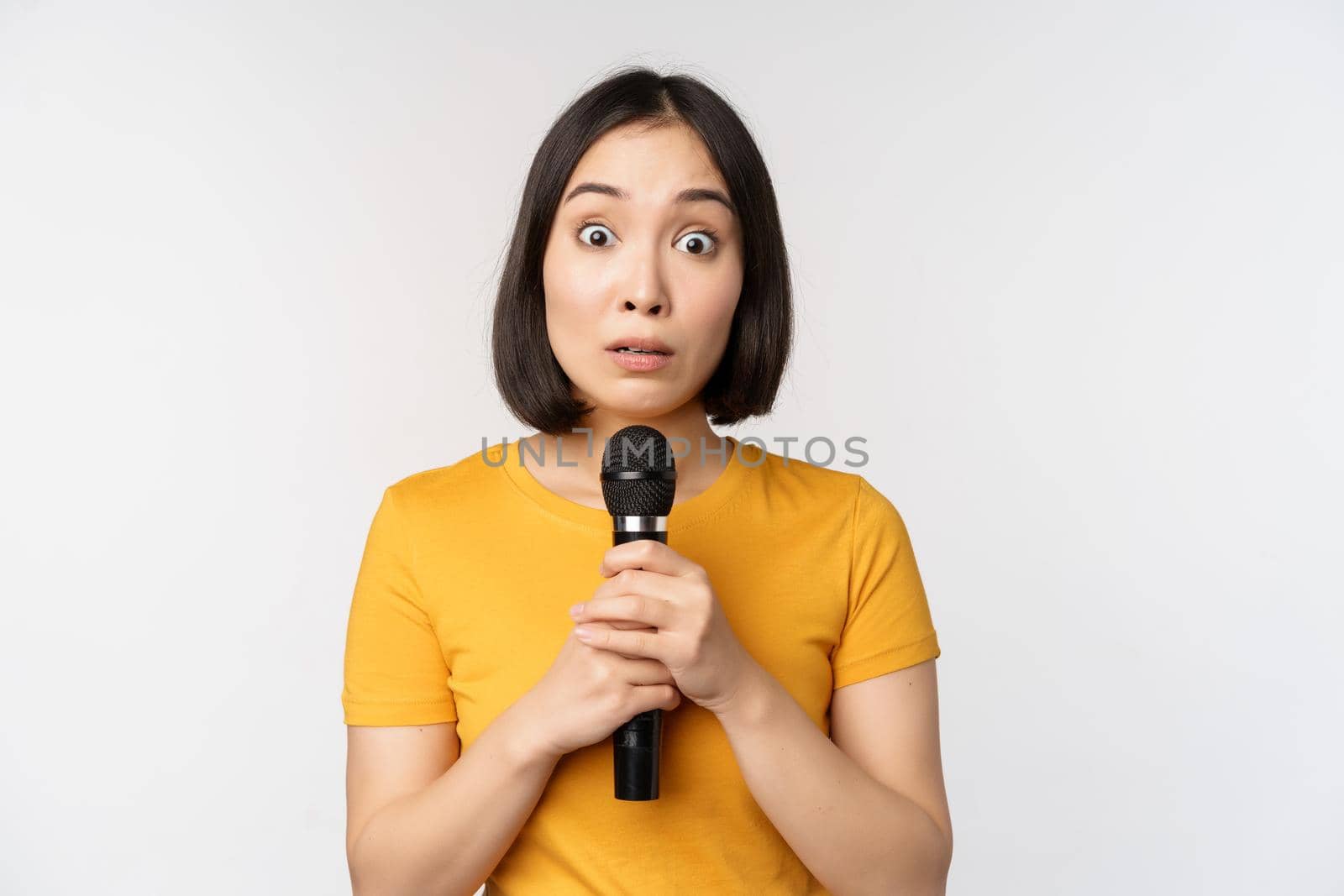 Modest asian girl holding microphone, scared talking in public, standing against white background by Benzoix