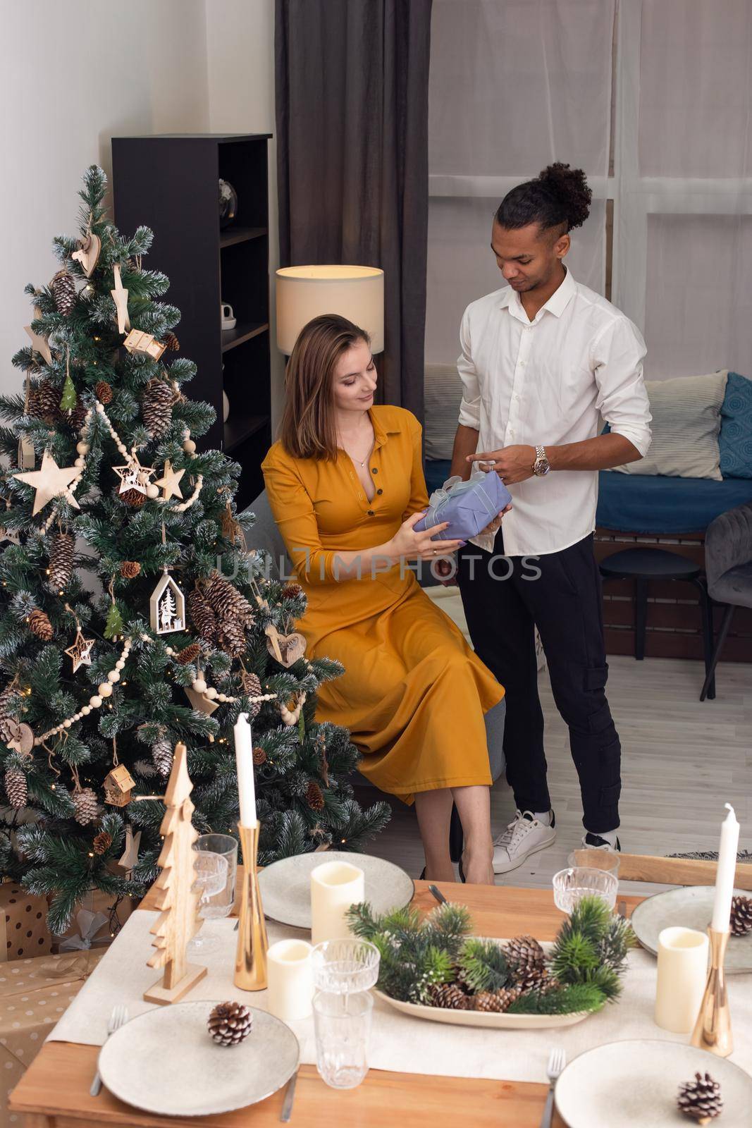 A young man in a white shirt and black pants, gives a lilac box with a gift to a young slender woman by Zakharova