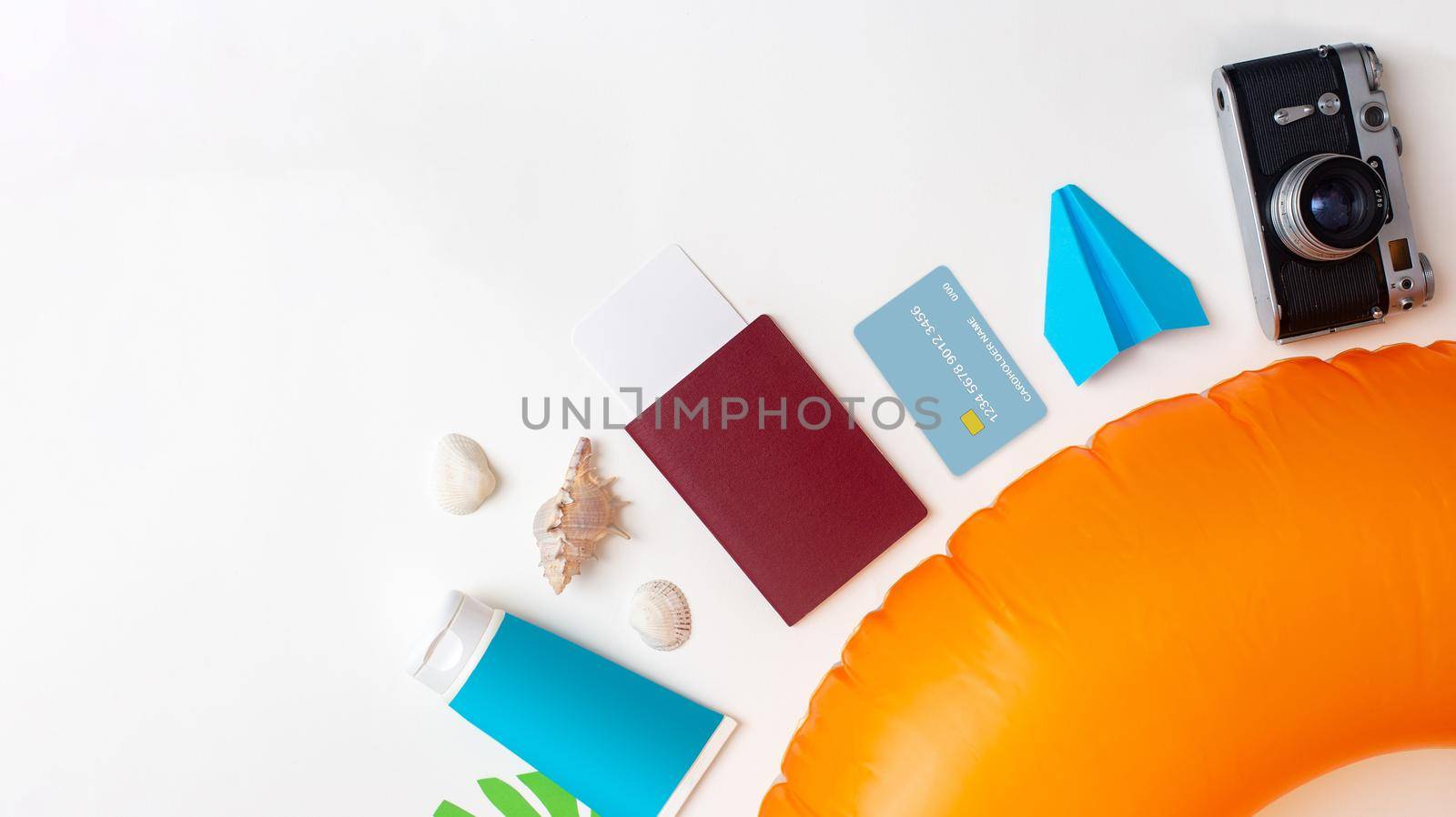 Summer travel set top view: orange swimming circle, passport, credit card, sun cream lies on white background. Copy space. Wide banner